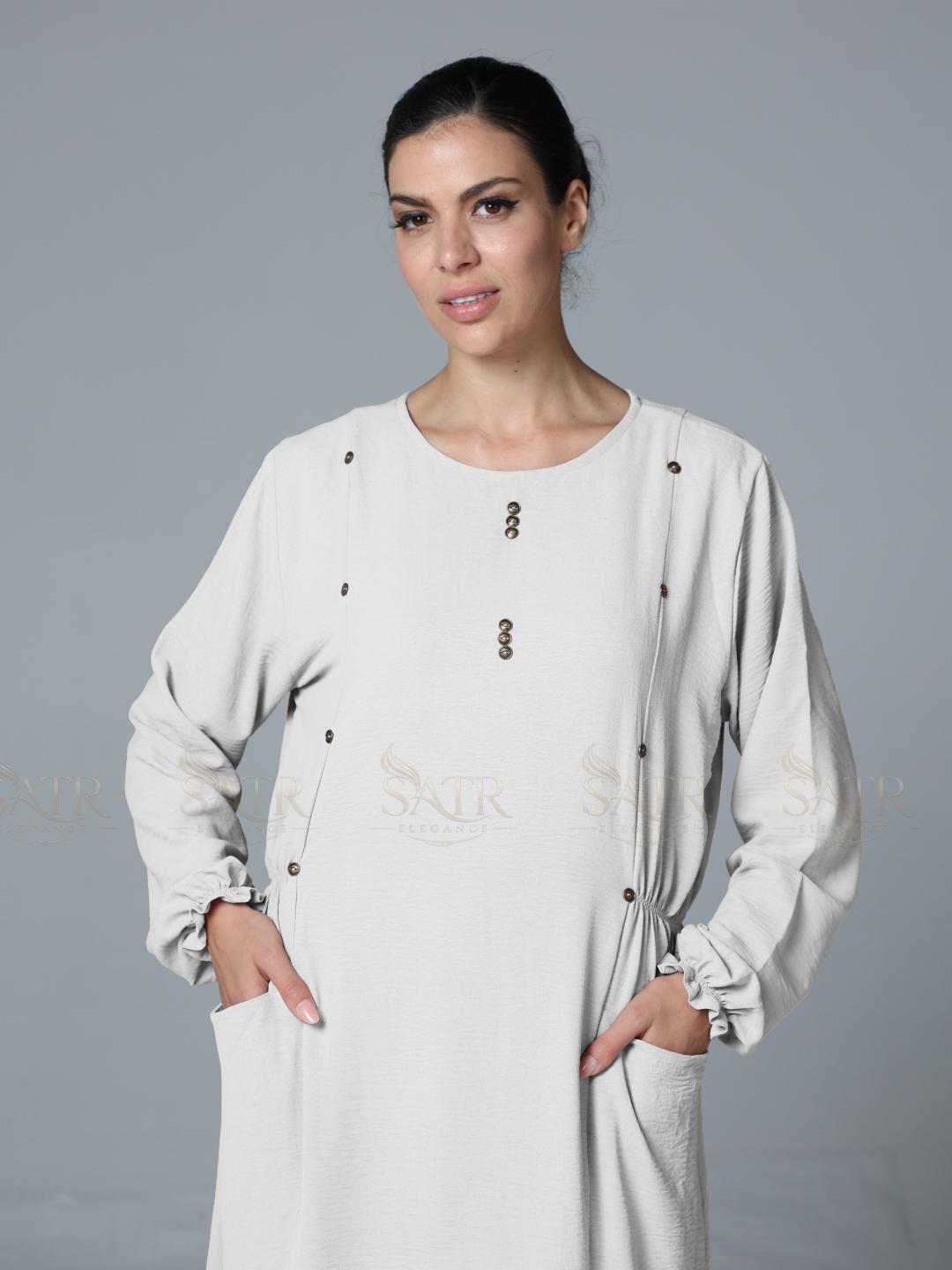 Woman wearing a off-white outfit with buttons against a gray background