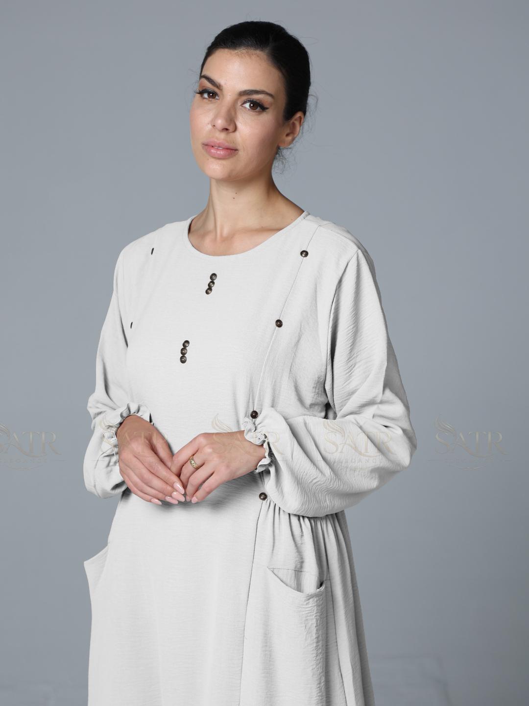 Woman wearing a off-white dress with black buttons on a gray background