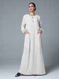 Woman wearing a long off-white abaya against a gray background