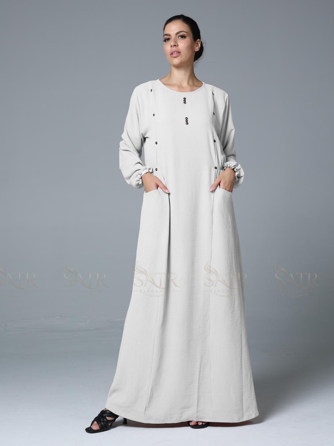 Woman wearing a long off-white abaya against a gray background