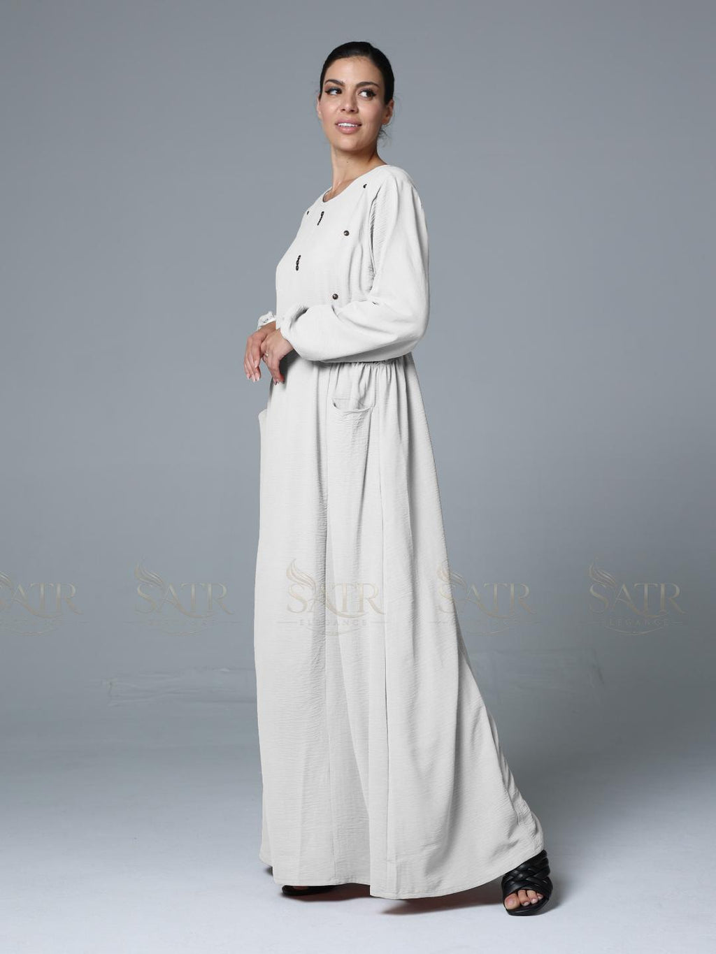 Woman wearing a long, light-colored dress against a gray background