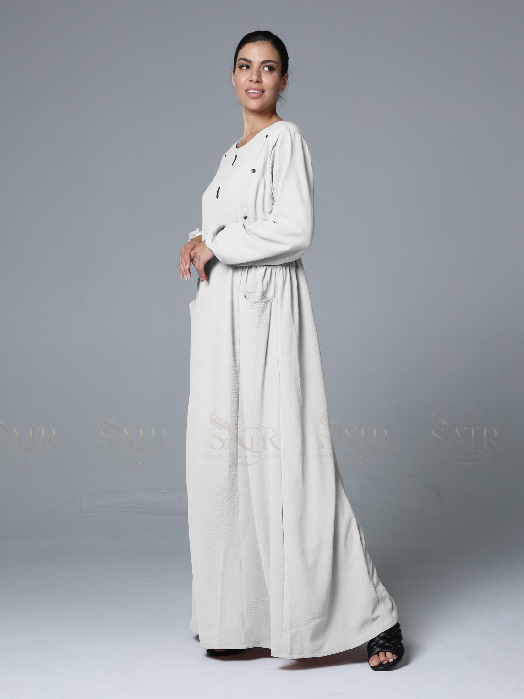 Woman wearing a long, light-colored dress against a gray background