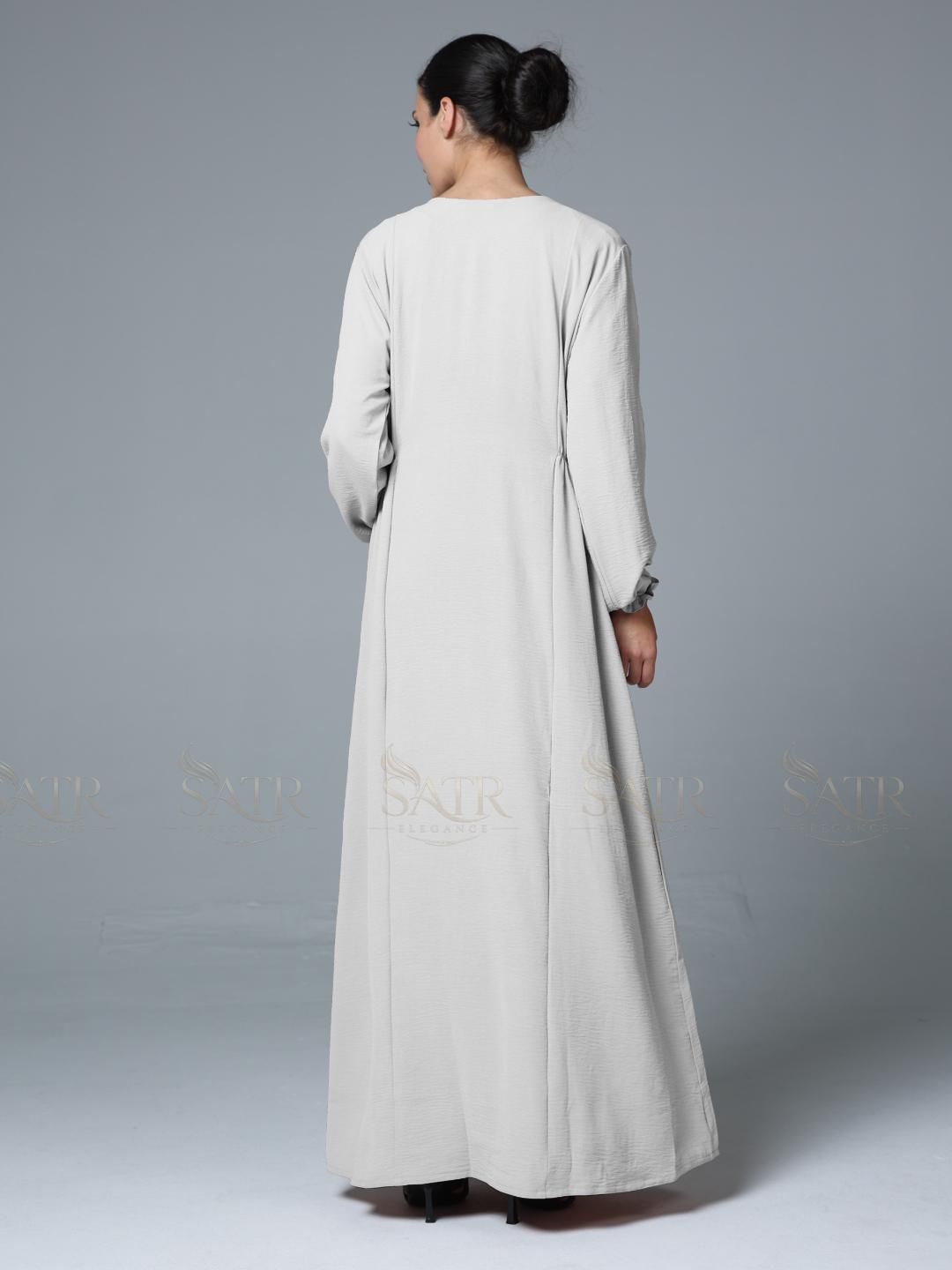 Woman wearing a long off-white dress against a gray background