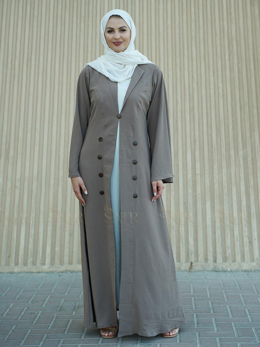 Woman wearing a long light brown coat over a white dress with a beige background
