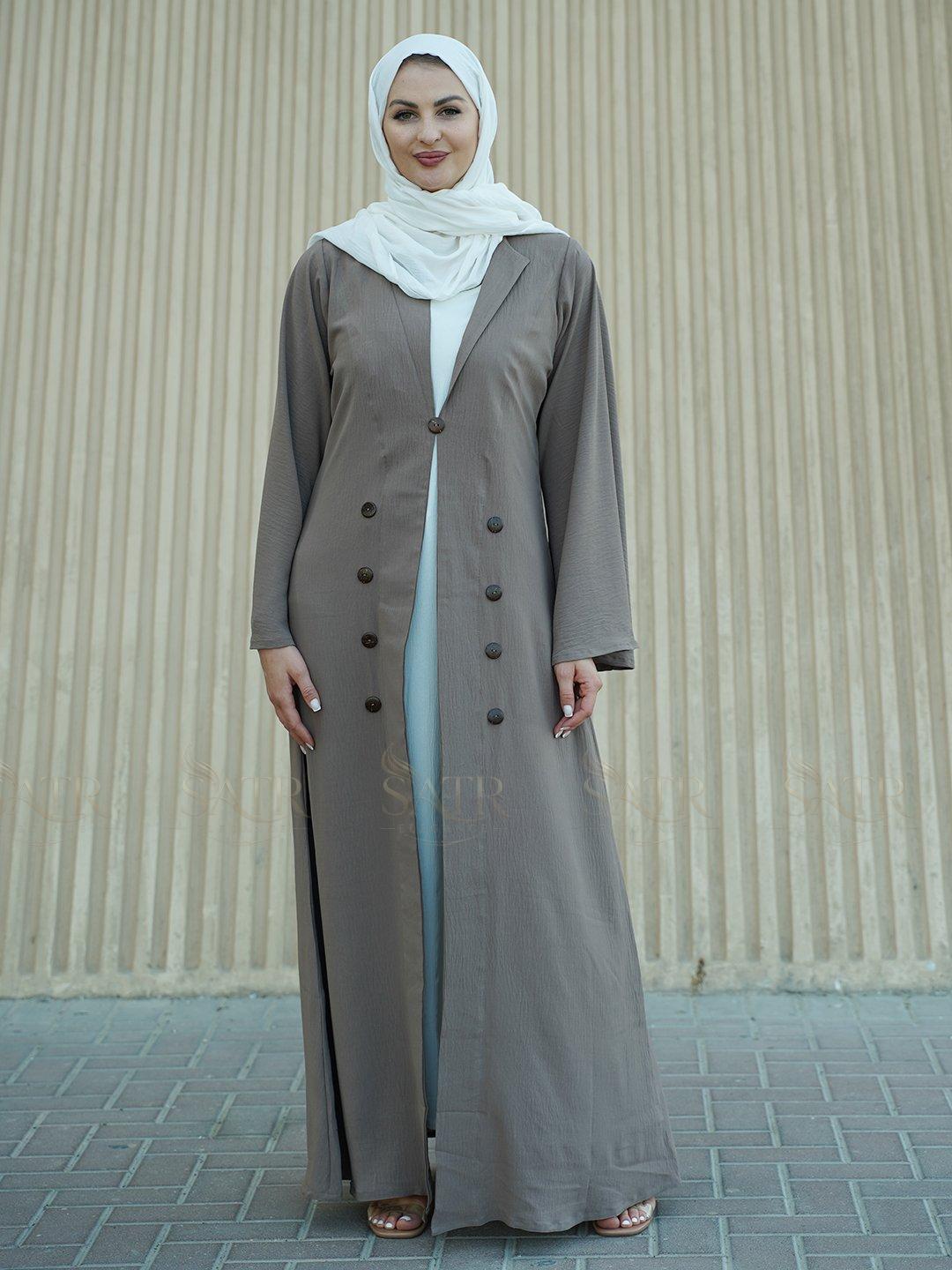Woman wearing a long light brown coat over a white dress with a beige background