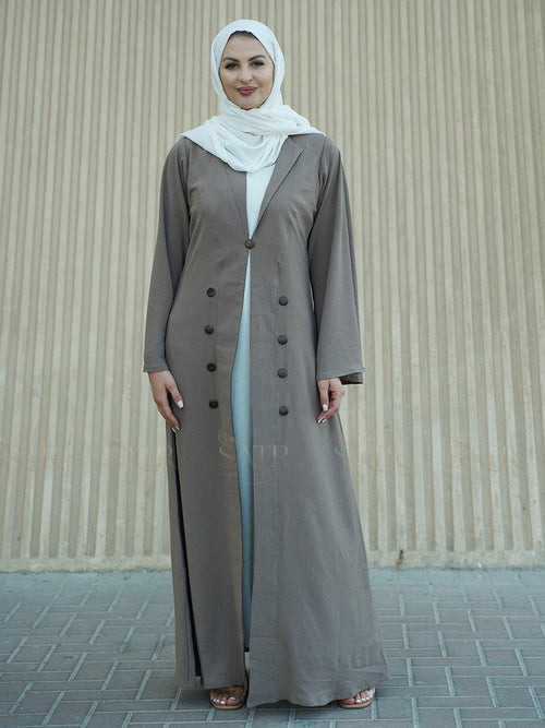 Woman wearing a long light brown coat over a white dress with a beige background