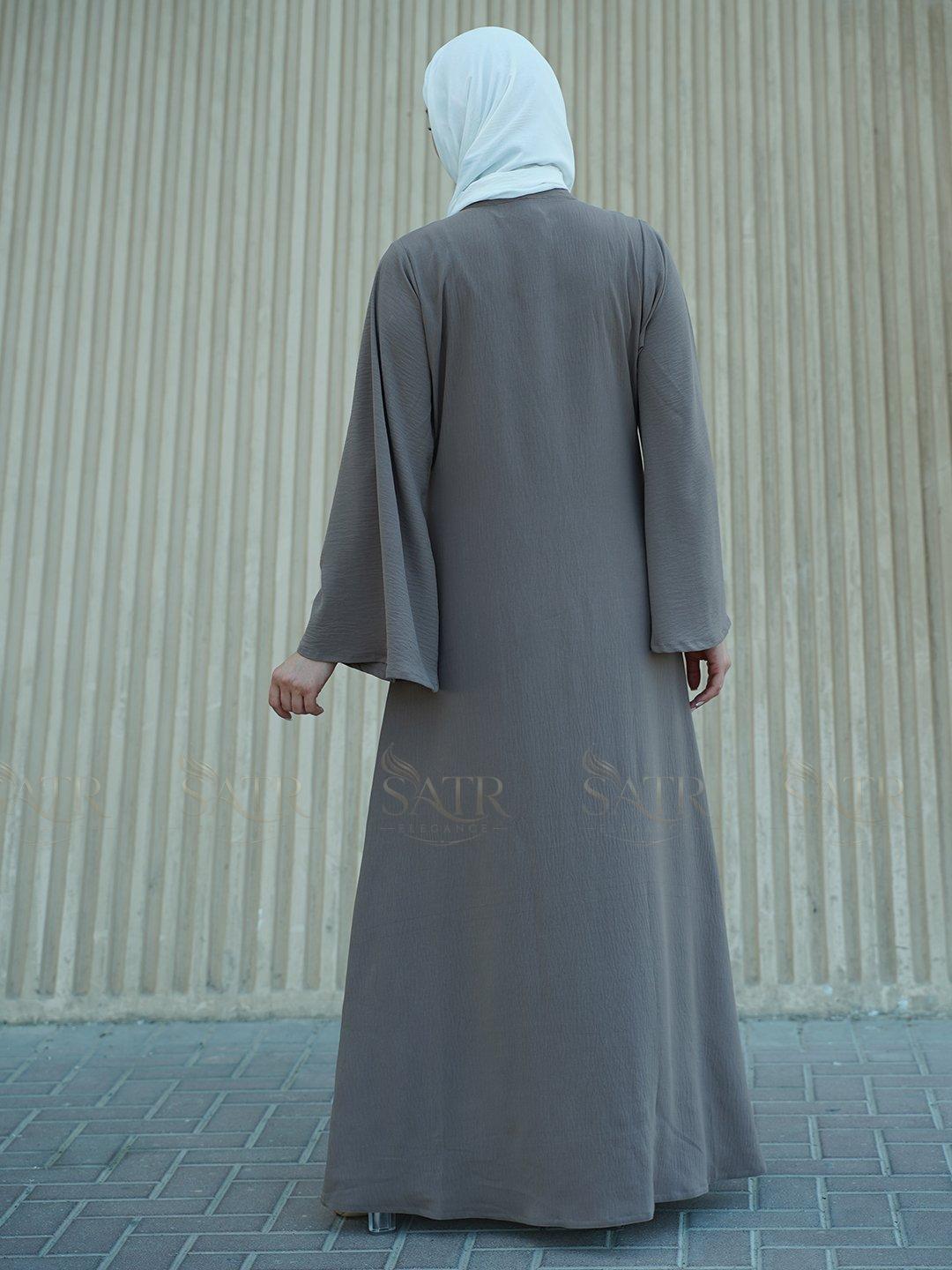 Person wearing a gray abaya with 'SATR' branding against a striped wall.