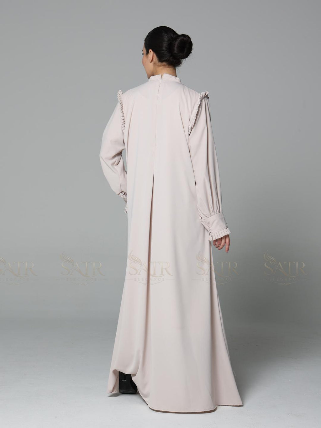 Woman wearing a long, light-colored dress against a gray background