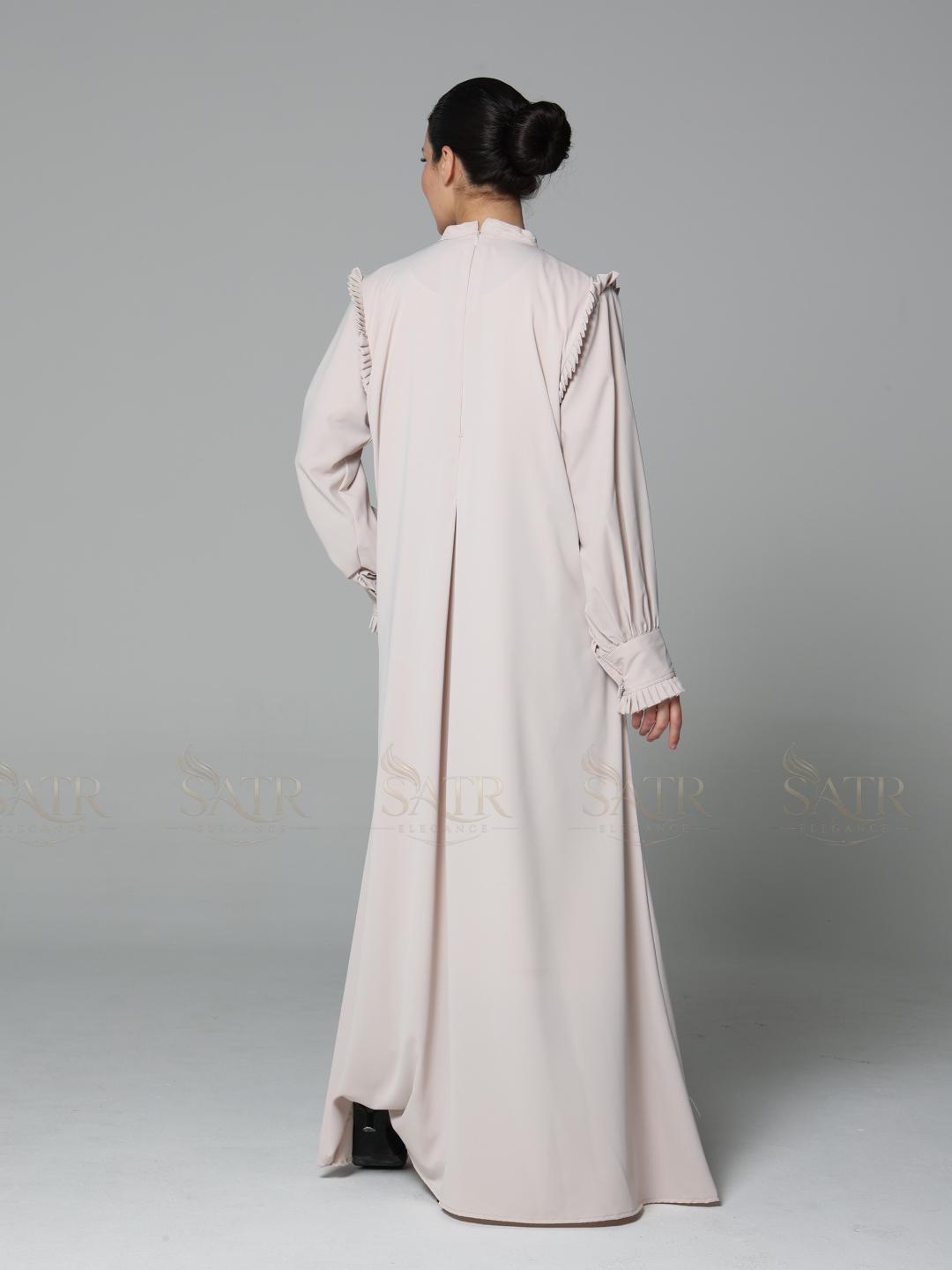 Woman wearing a long, light-colored dress against a gray background