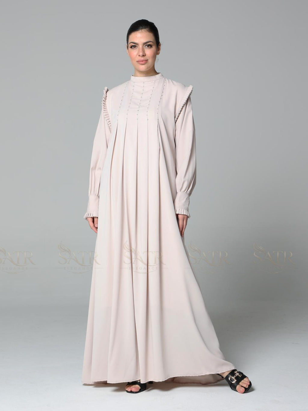 Woman wearing a light pink abaya on a gray background