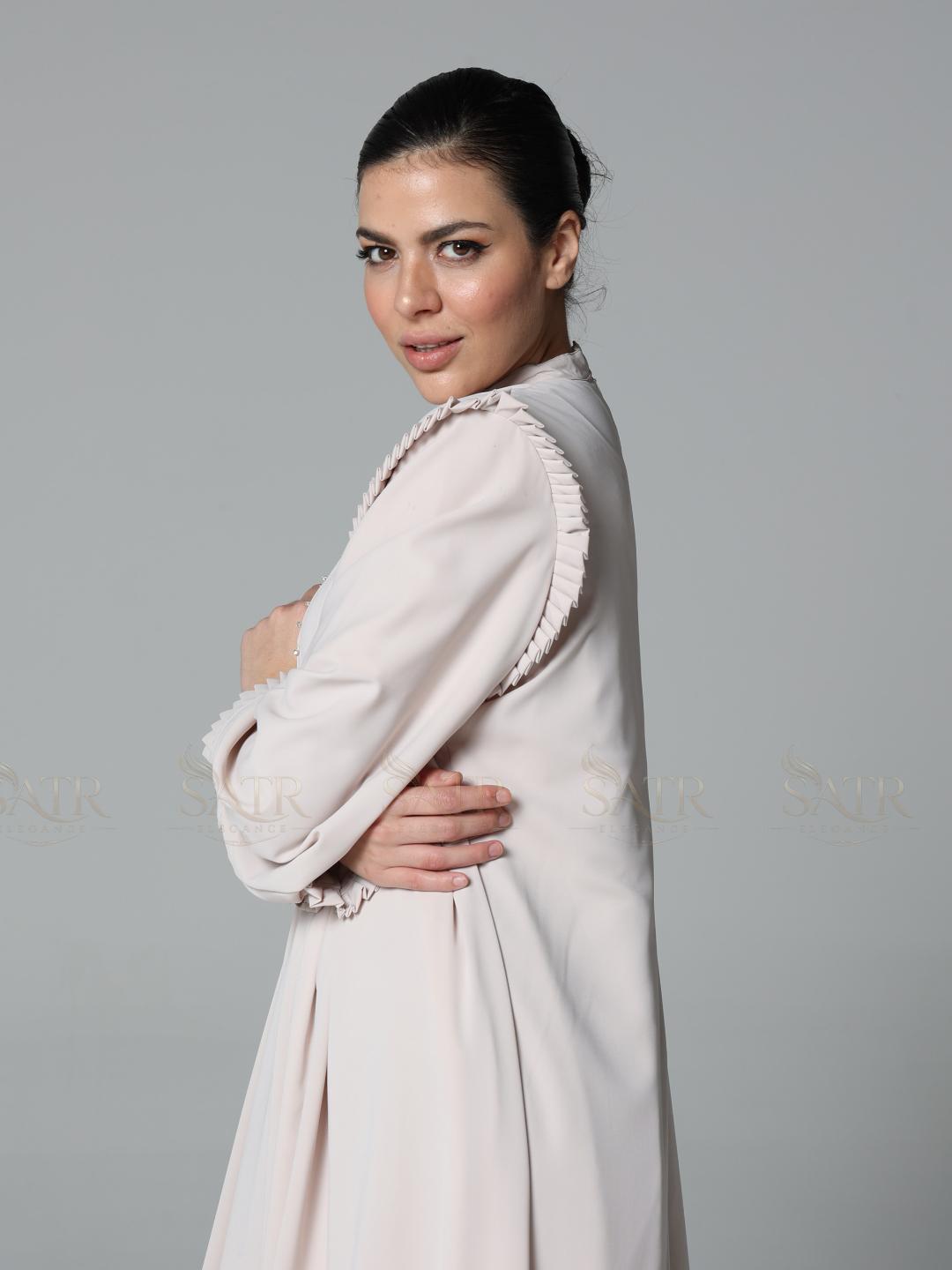 Woman wearing a light pink dress with ruffled sleeves against a gray background
