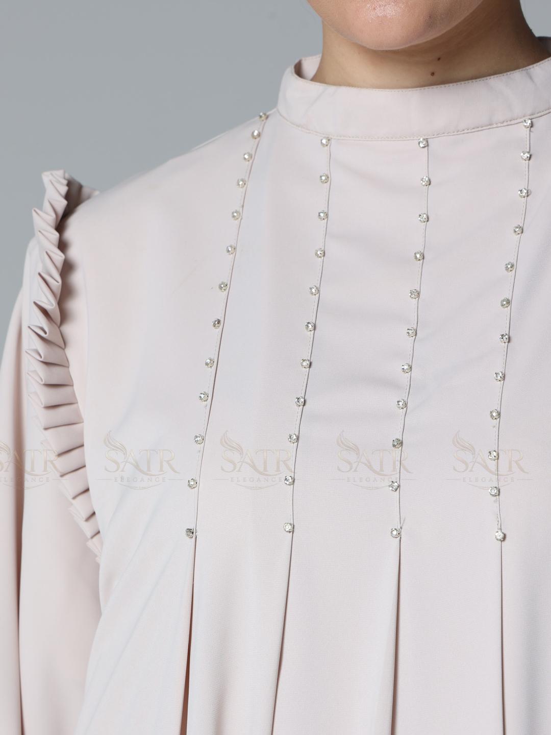 Close-up of a light pink blouse with pearl embellishments on a gray background