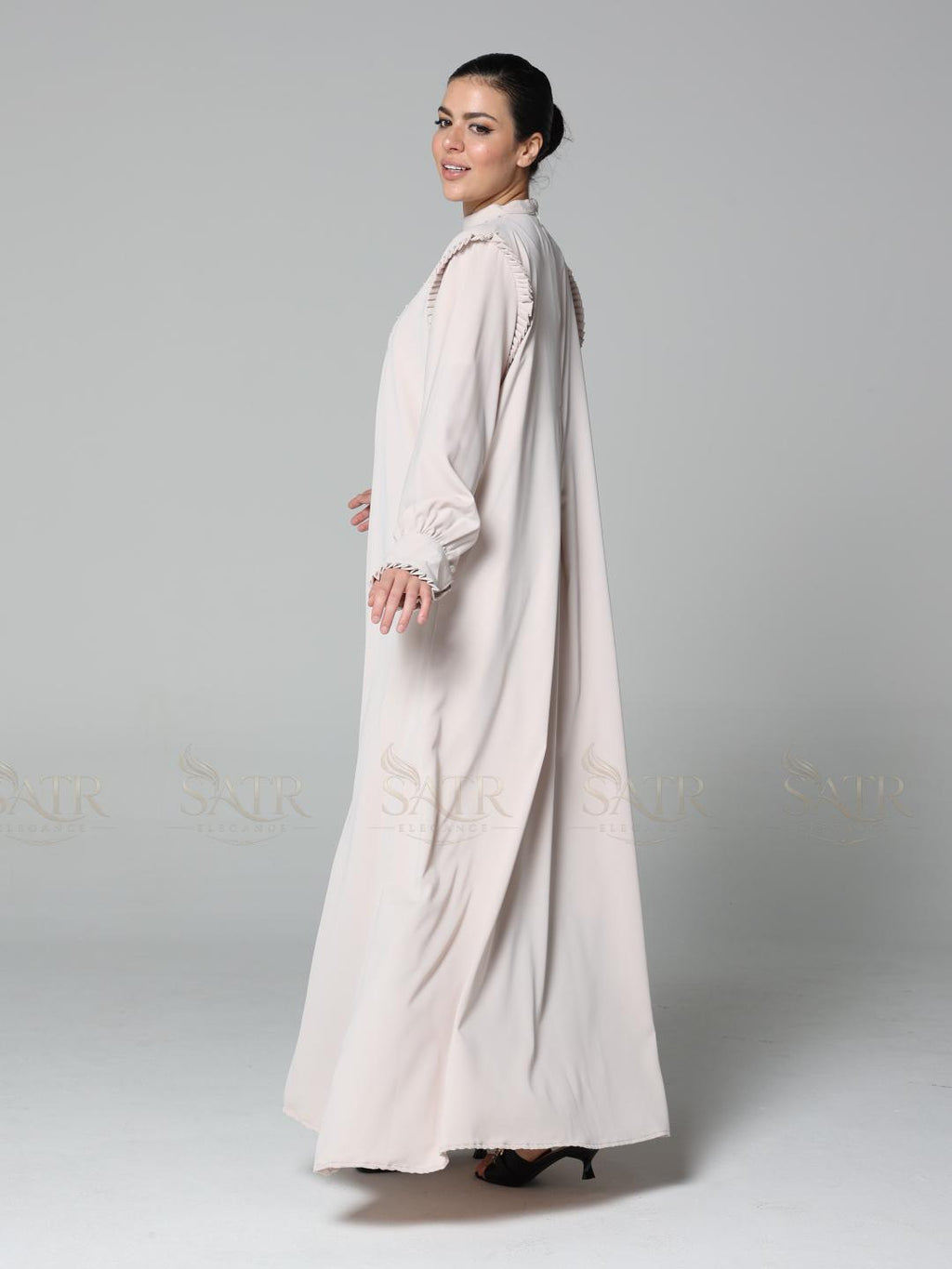 Woman wearing a long, light-colored dress against a plain background