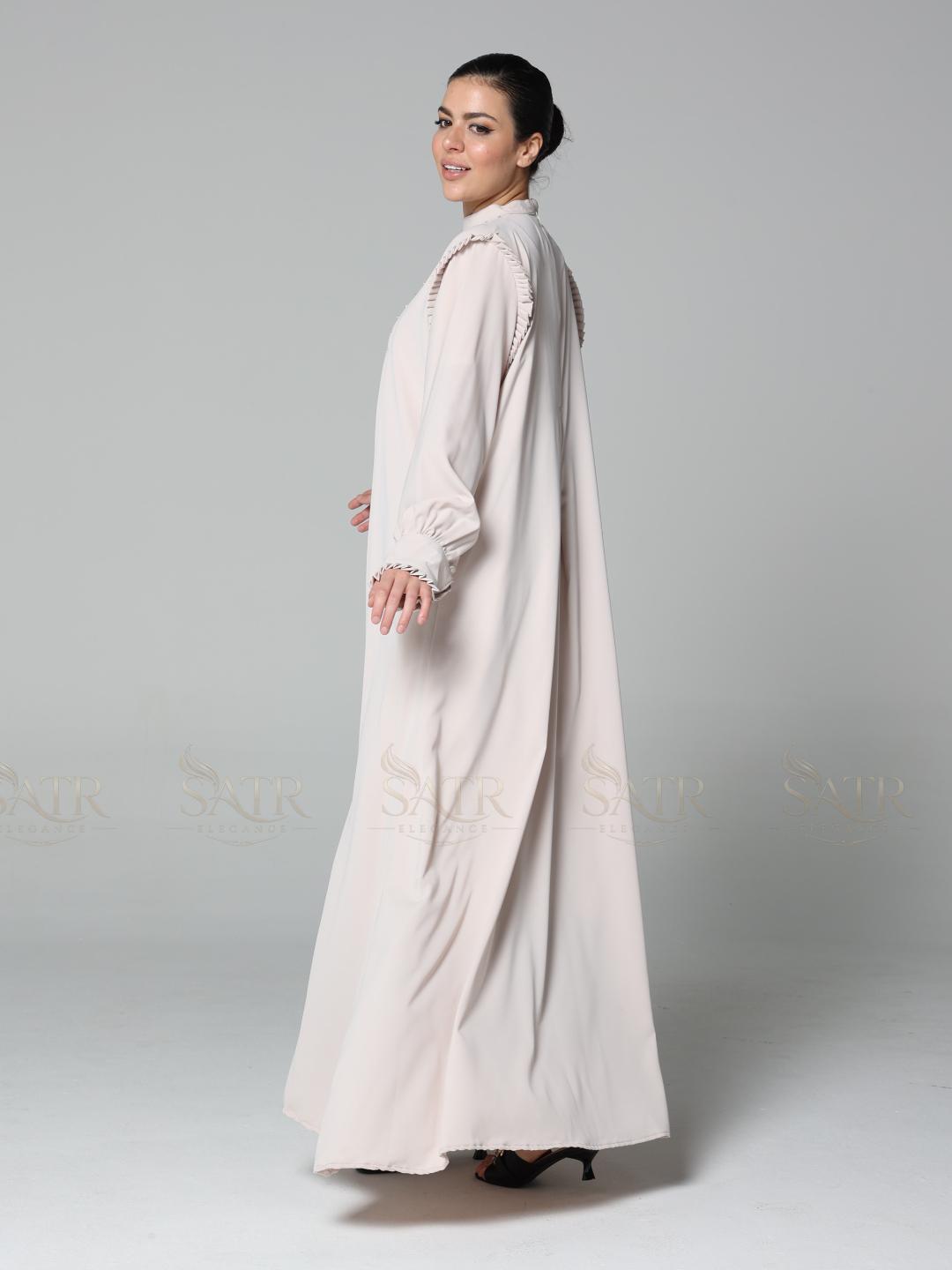 Woman wearing a long, light-colored dress against a plain background