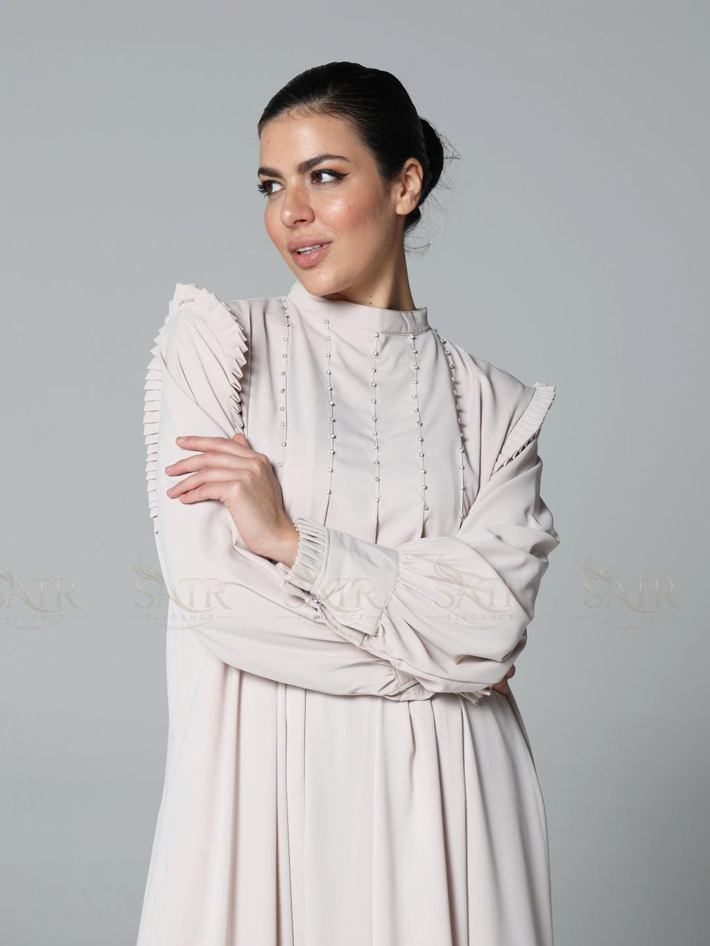 Woman wearing a light pink dress with ruffled sleeves against a gray background