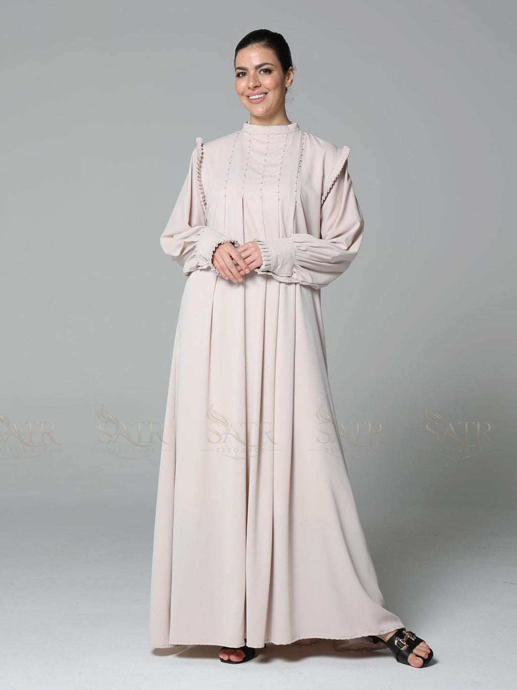 Woman wearing a long, light-colored dress against a gray background
