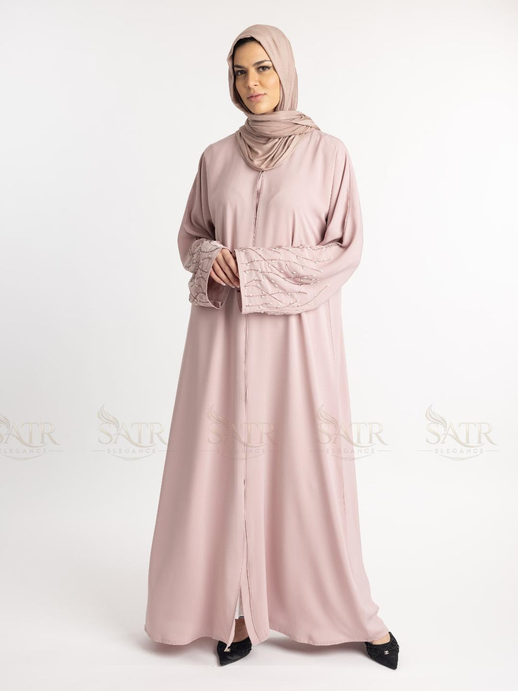 Woman wearing a light pink abaya with a matching hijab on a white background