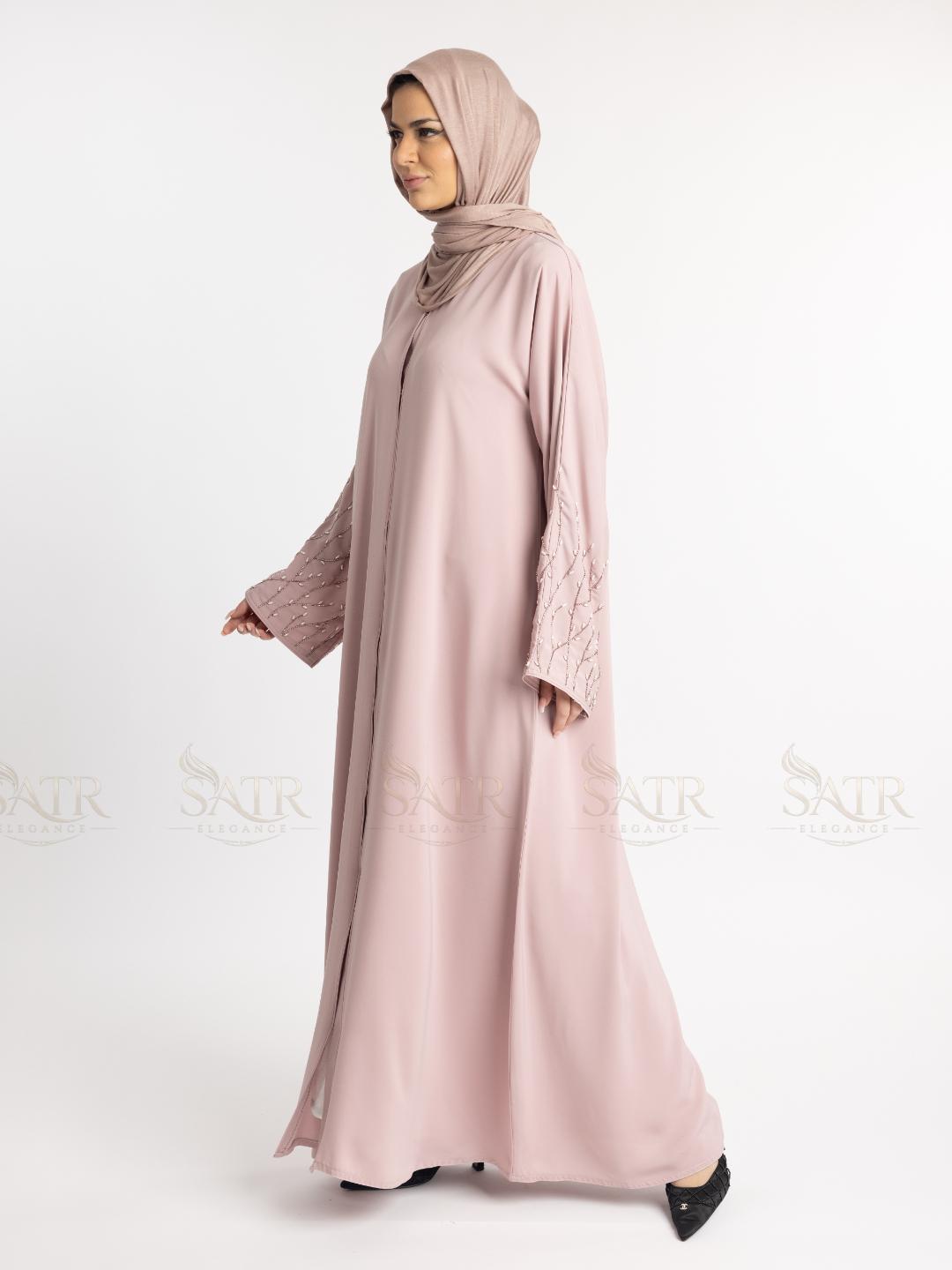 Woman wearing a light pink abaya with a matching hijab on a white background