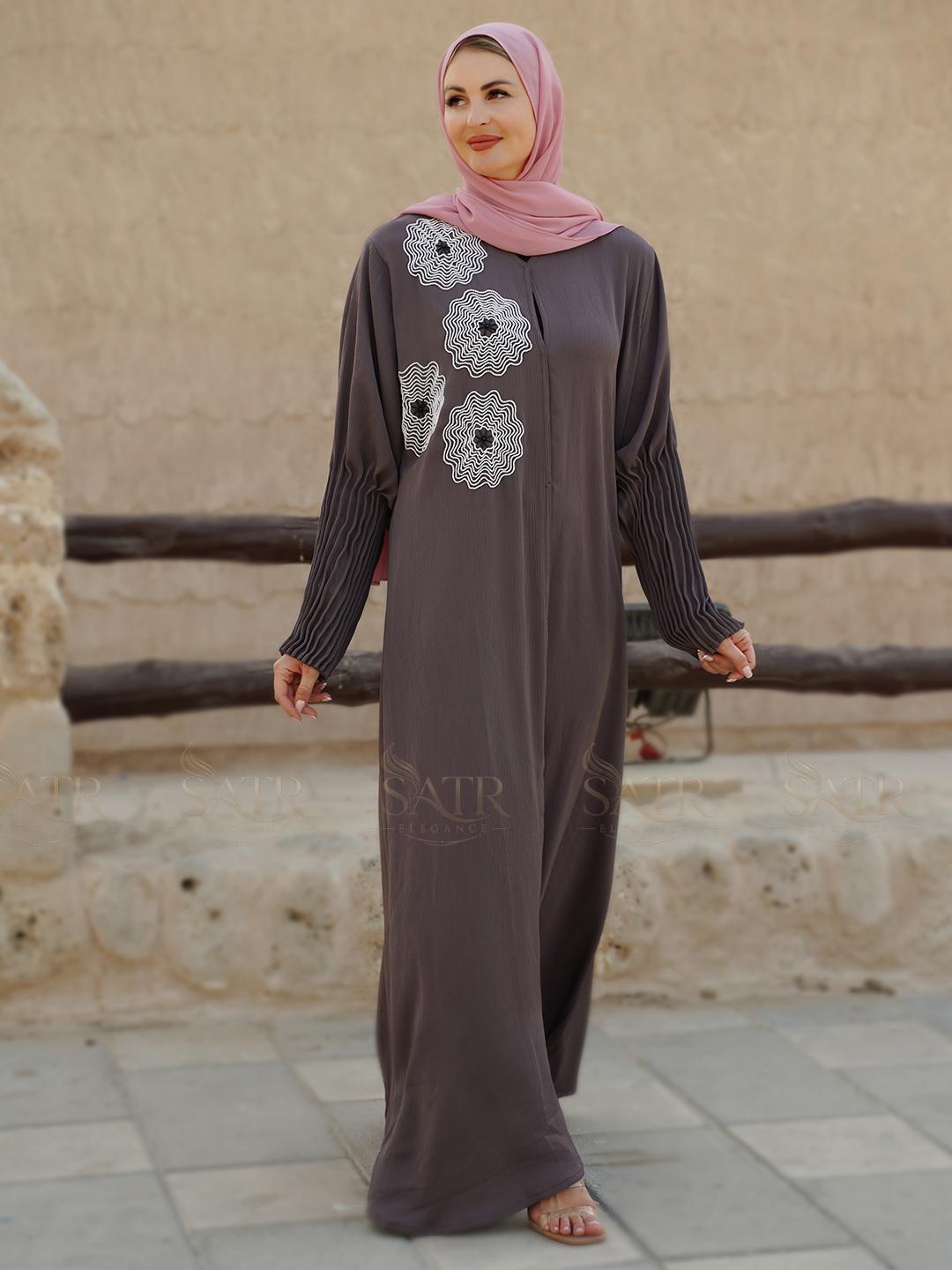 Woman wearing a long, dark gray dress with floral patterns in an outdoor setting.