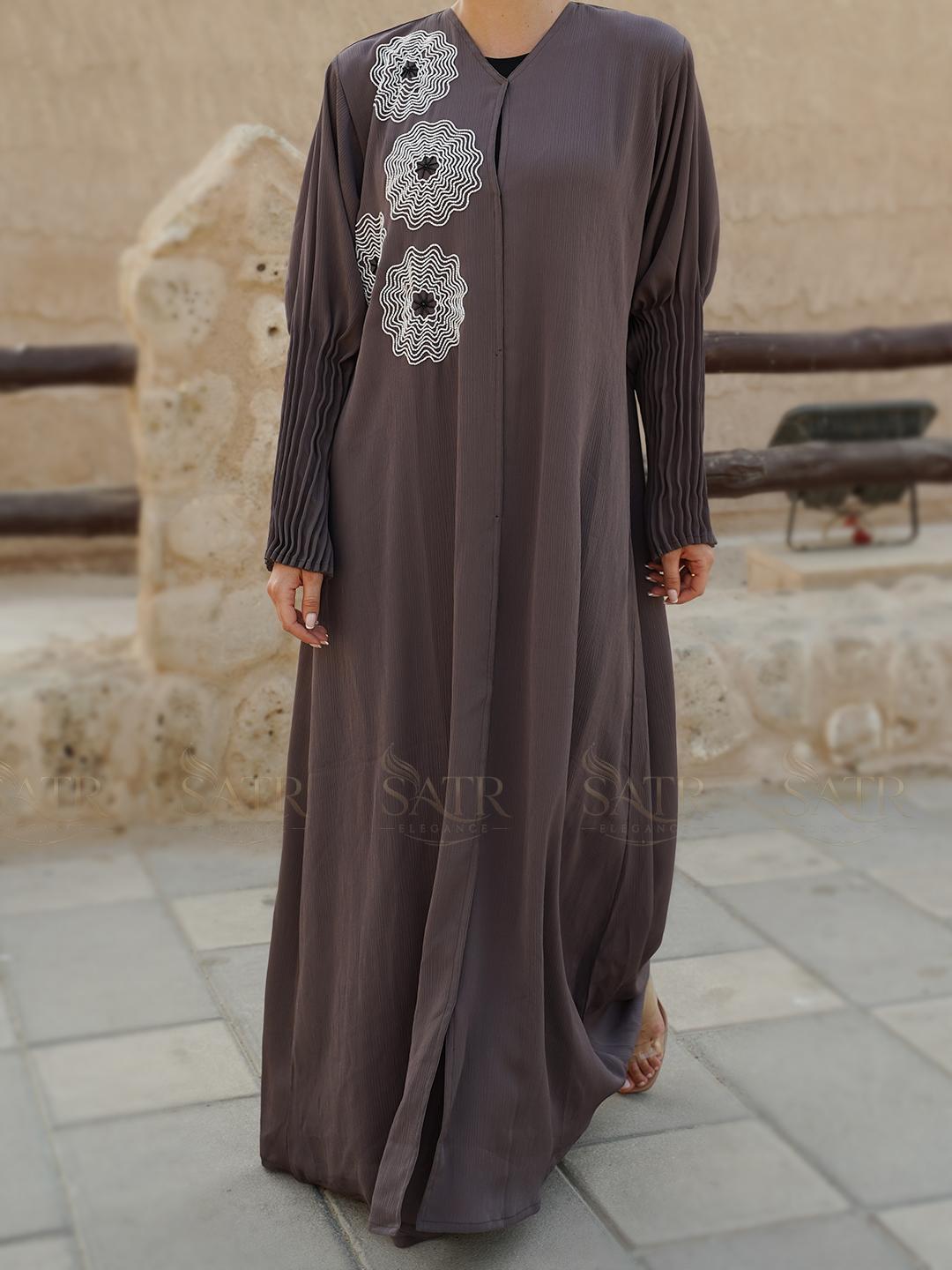 Long brown dress with floral embroidery on a stone pavement background
