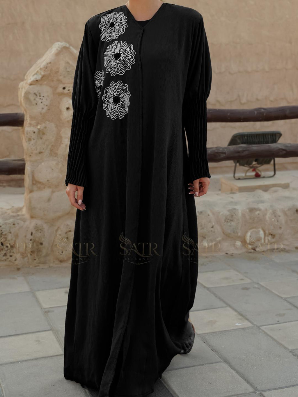 Black dress with white floral embroidery worn by a person, standing on a stone pavement.