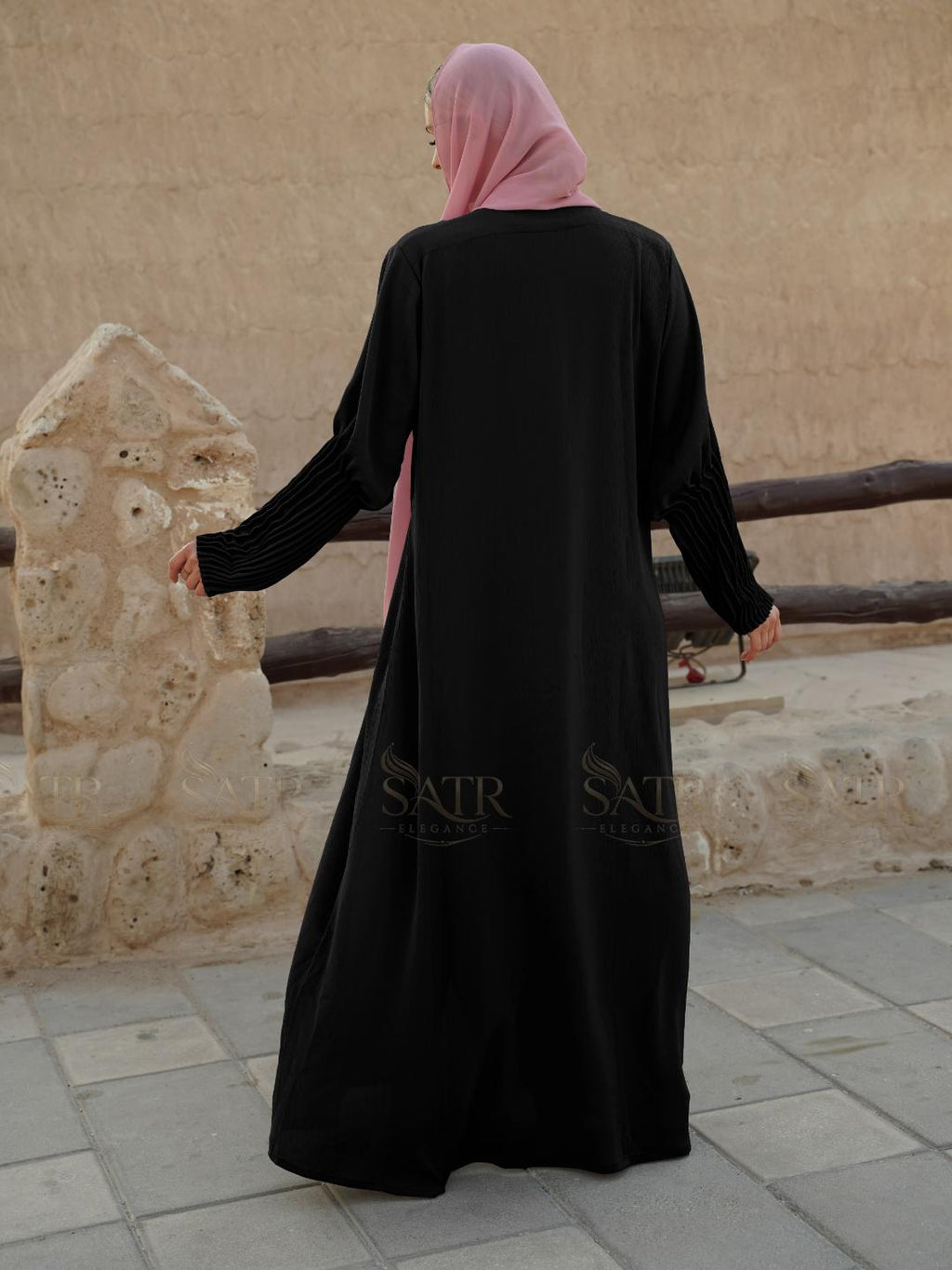 Person wearing a black abaya with pink hijab in an outdoor setting