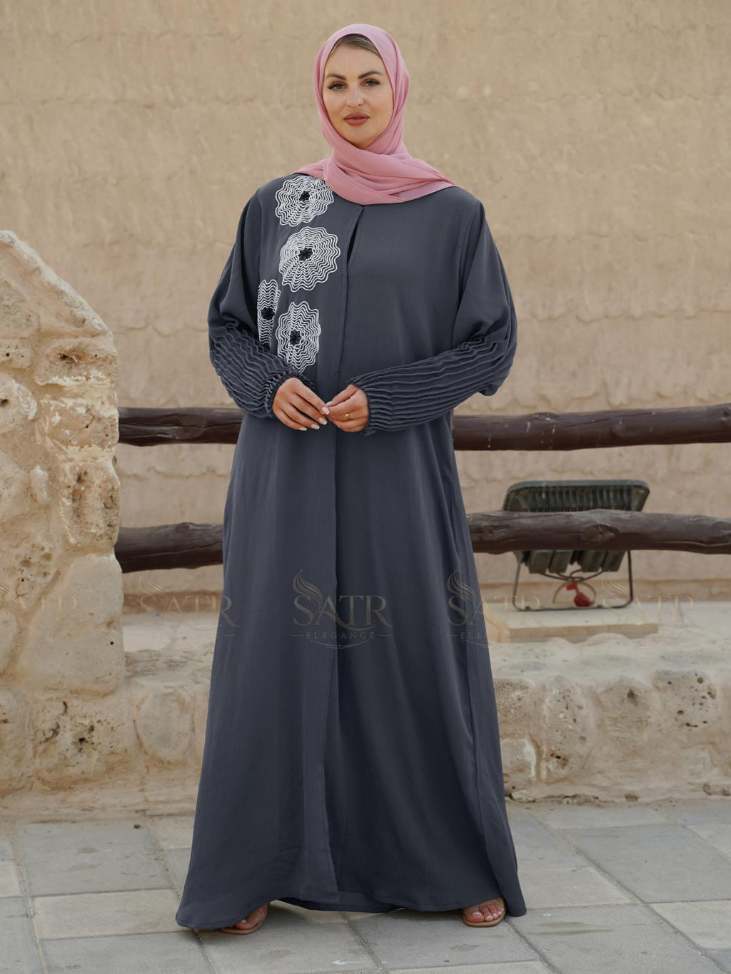 Woman wearing a long dark gray dress with floral patterns in an outdoor setting.