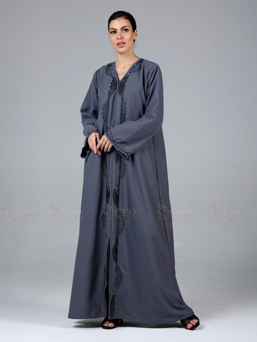 Woman wearing a long gray dress with intricate detailing on a plain background