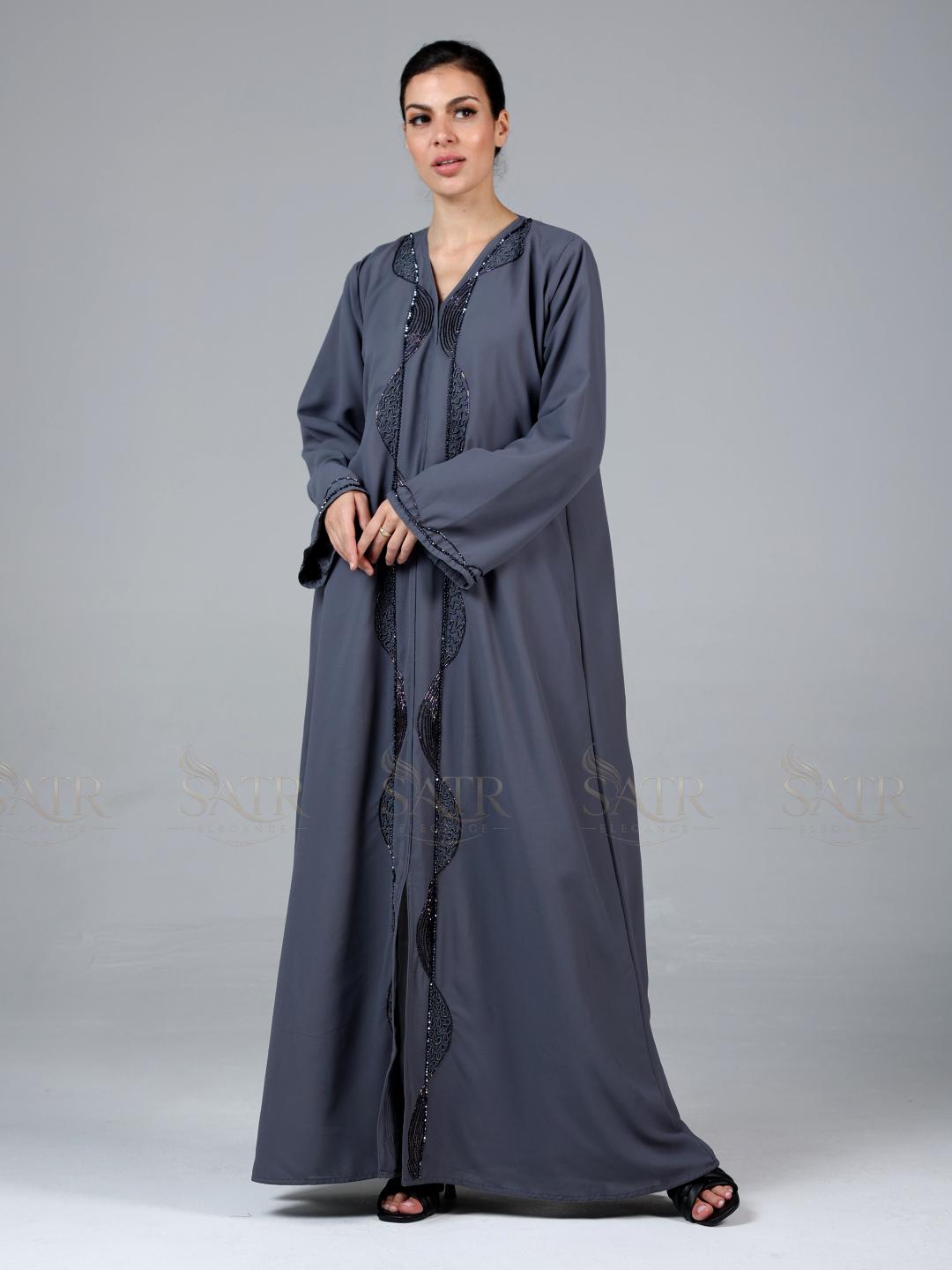 Woman wearing a long gray dress with intricate detailing on a plain background