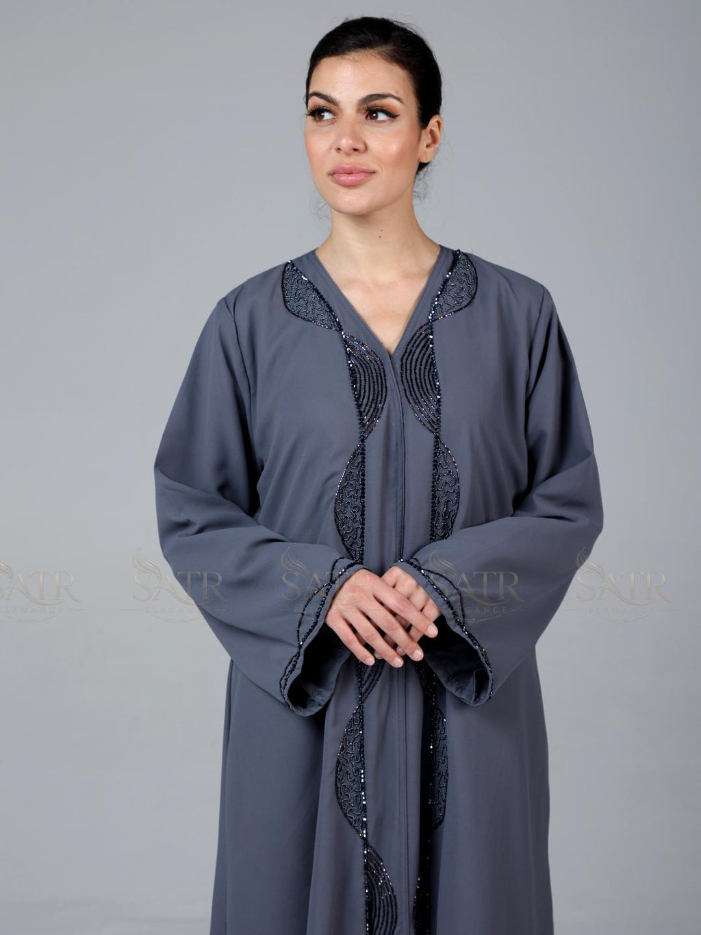 Woman wearing a gray abaya with black embroidery on a gray background