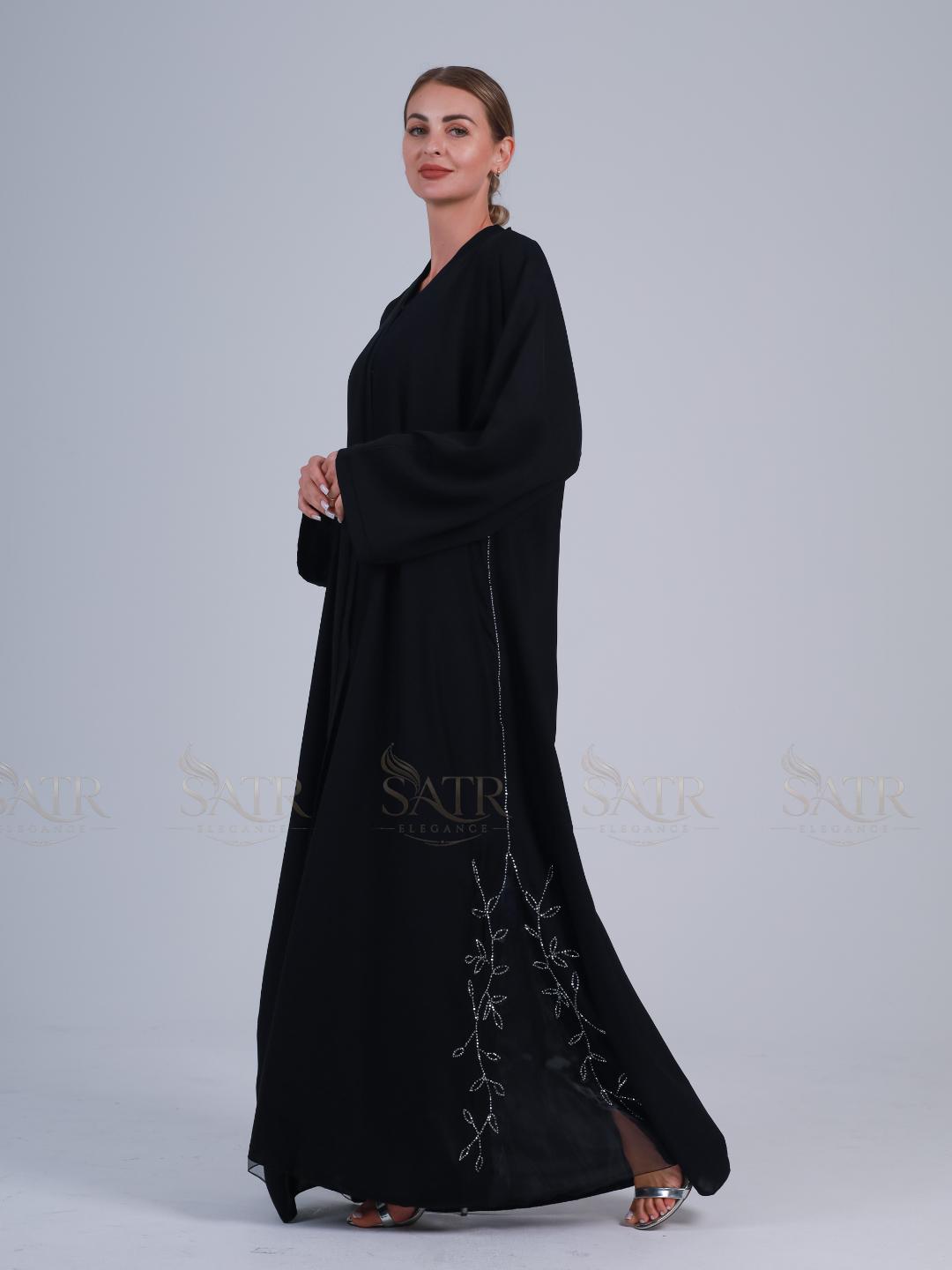 Woman wearing a black abaya with floral embroidery on a light gray background
