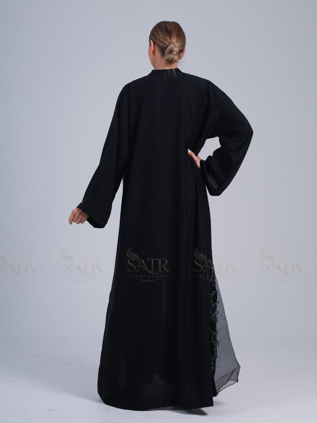 Person wearing a black long-sleeve dress with lace details on a white background