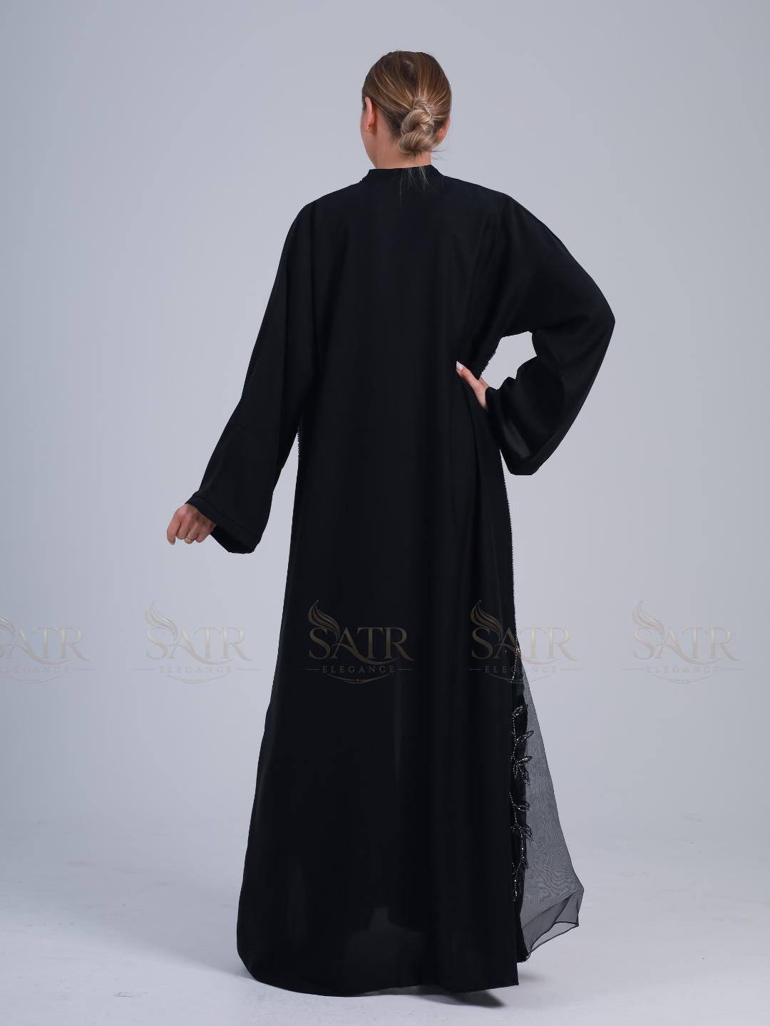 Person wearing a black long-sleeve dress with lace details on a white background