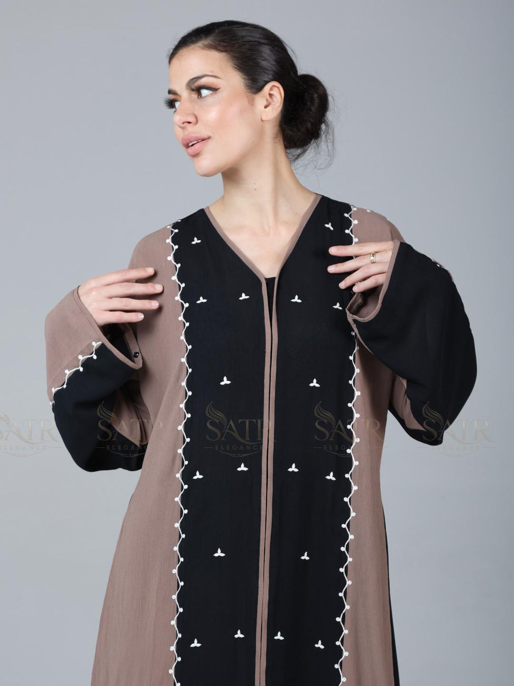 Woman wearing a black and brown dress with intricate detailing on a gray background
