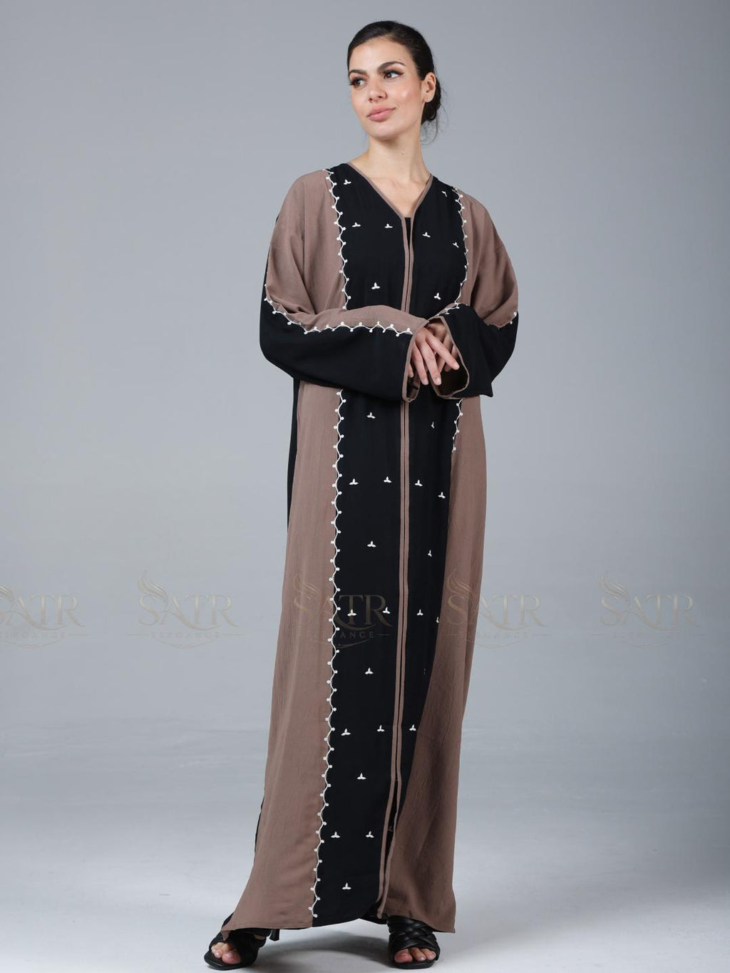Woman wearing a long, brown and black dress with star patterns on a gray background