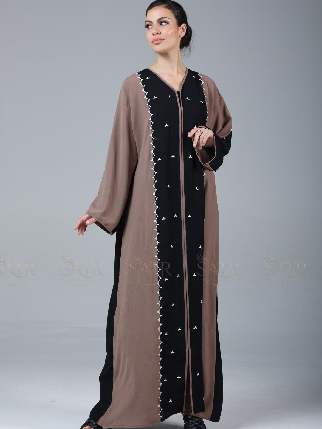 Woman wearing a long, brown and black dress with white embroidery on a gray background