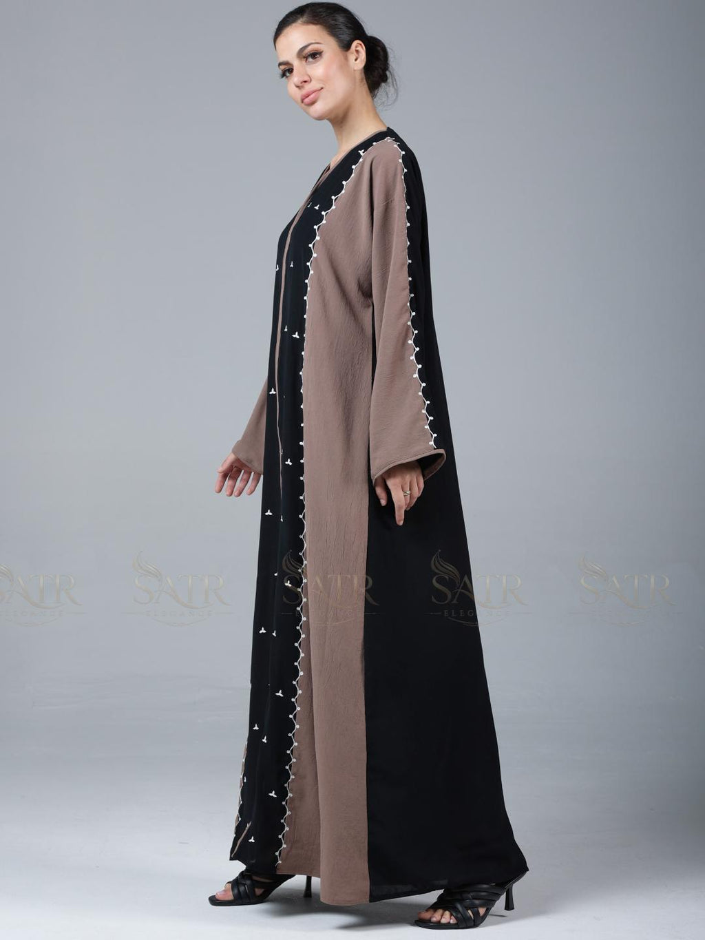 Woman wearing a black and brown abaya with star patterns on a gray background