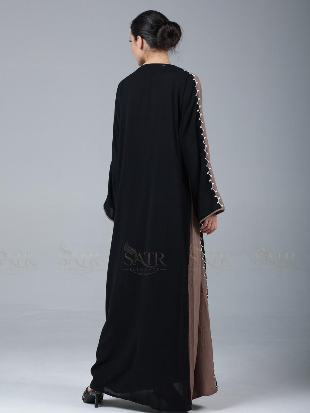 Woman wearing a black abaya with brown trim on a gray background