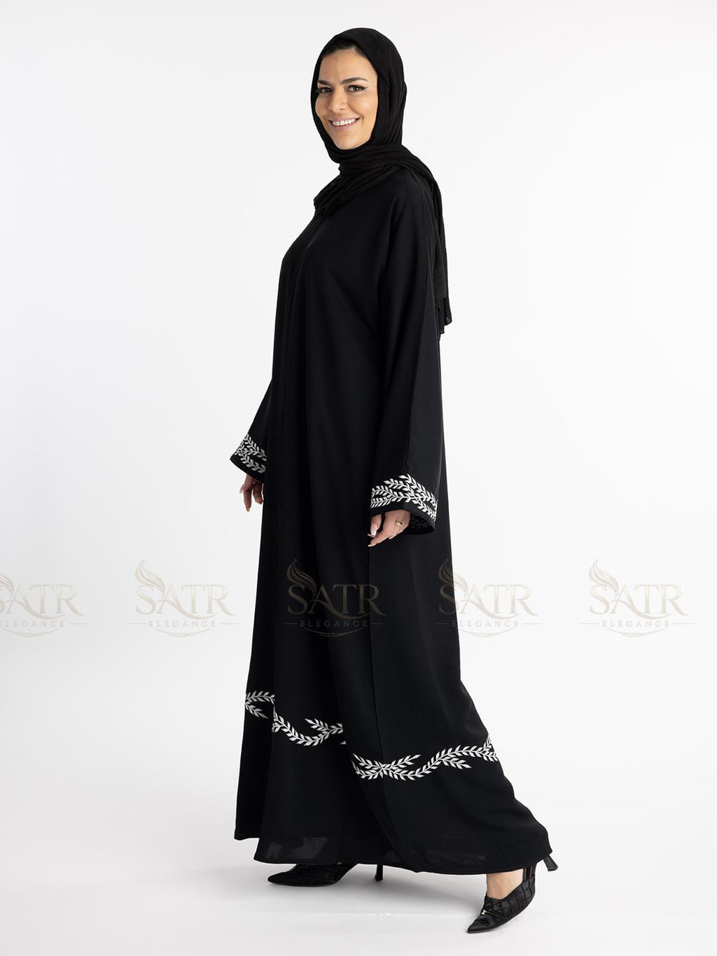 Woman wearing a premium black abaya with white embroidery on a white background