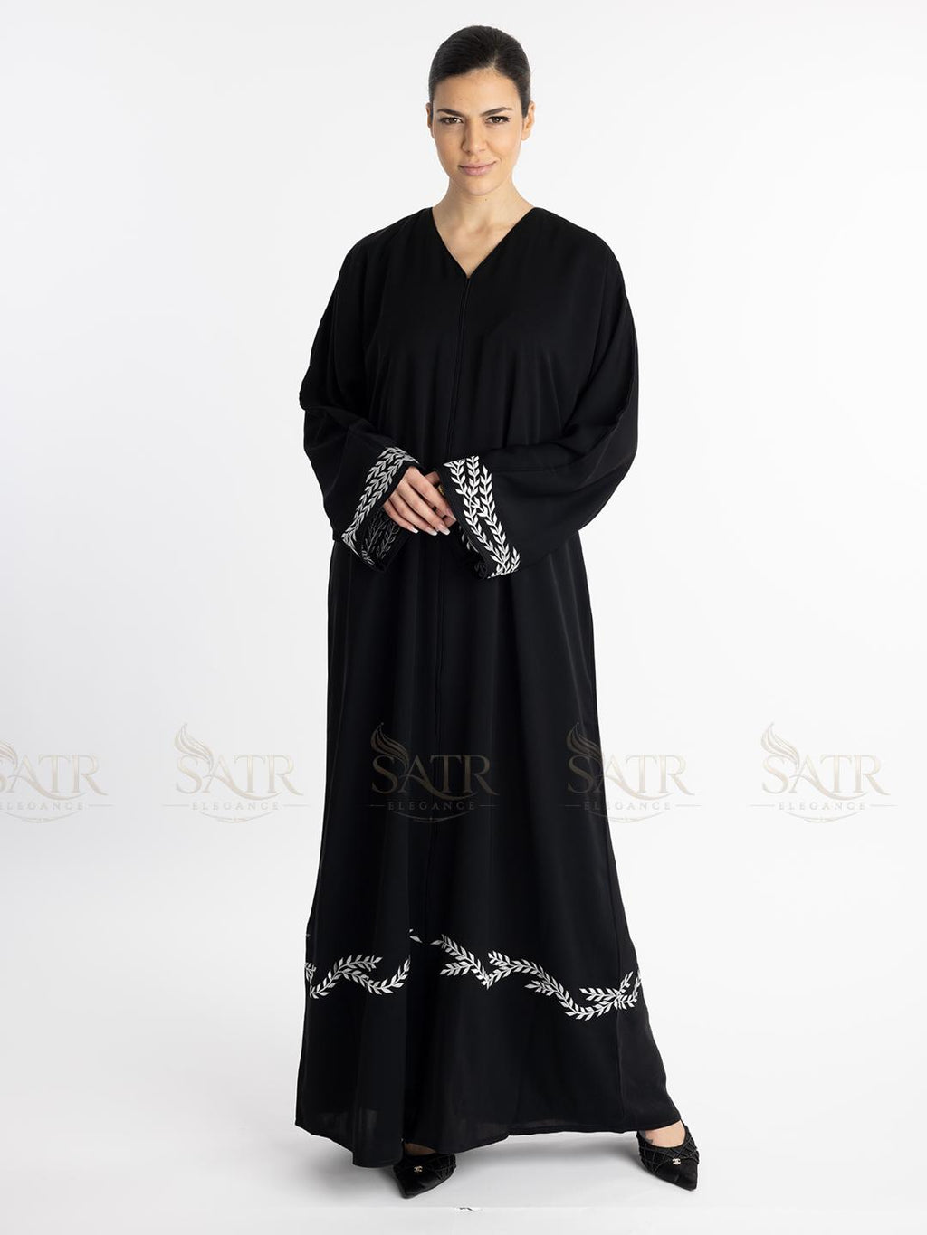 Woman wearing a premium black abaya with white embroidery on a white background
