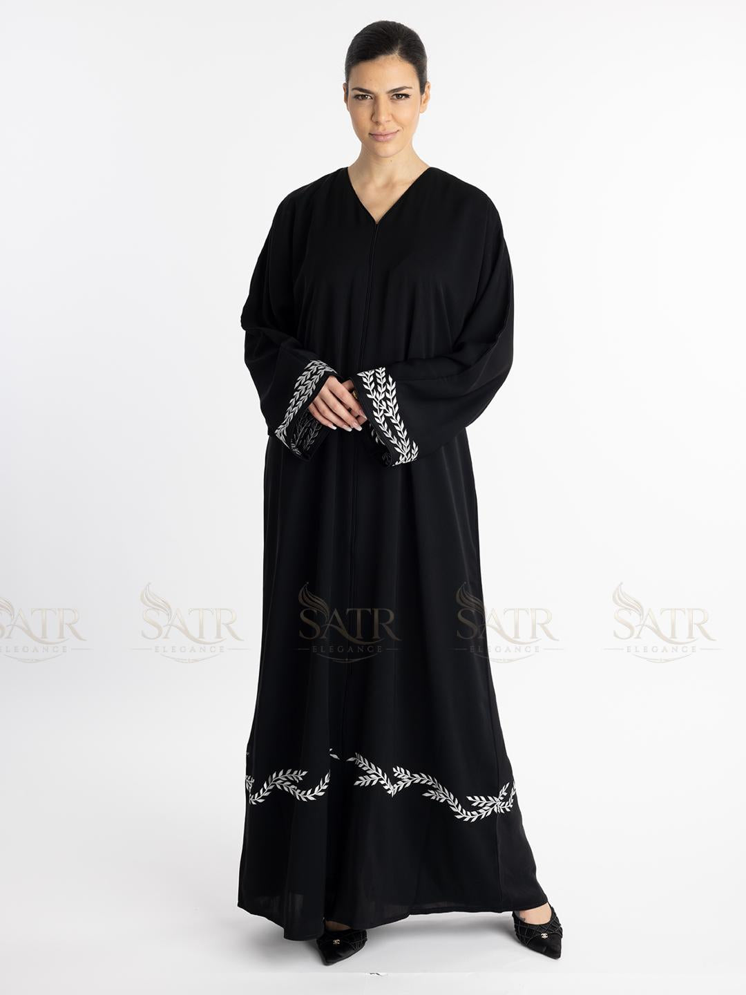 Woman wearing a premium black abaya with white embroidery on a white background