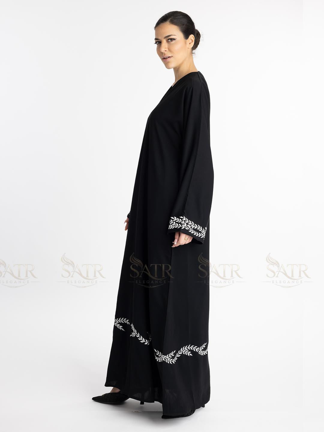 Woman wearing a premium black abaya with white embroidery on a white background