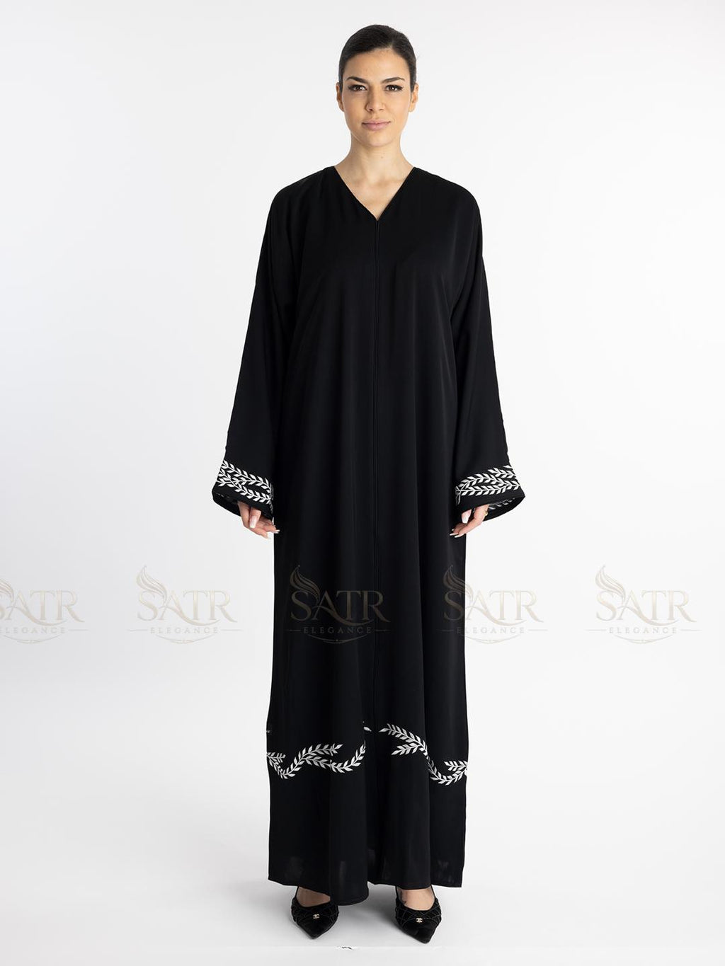 Woman wearing a premium black abaya with white embroidery on a white background