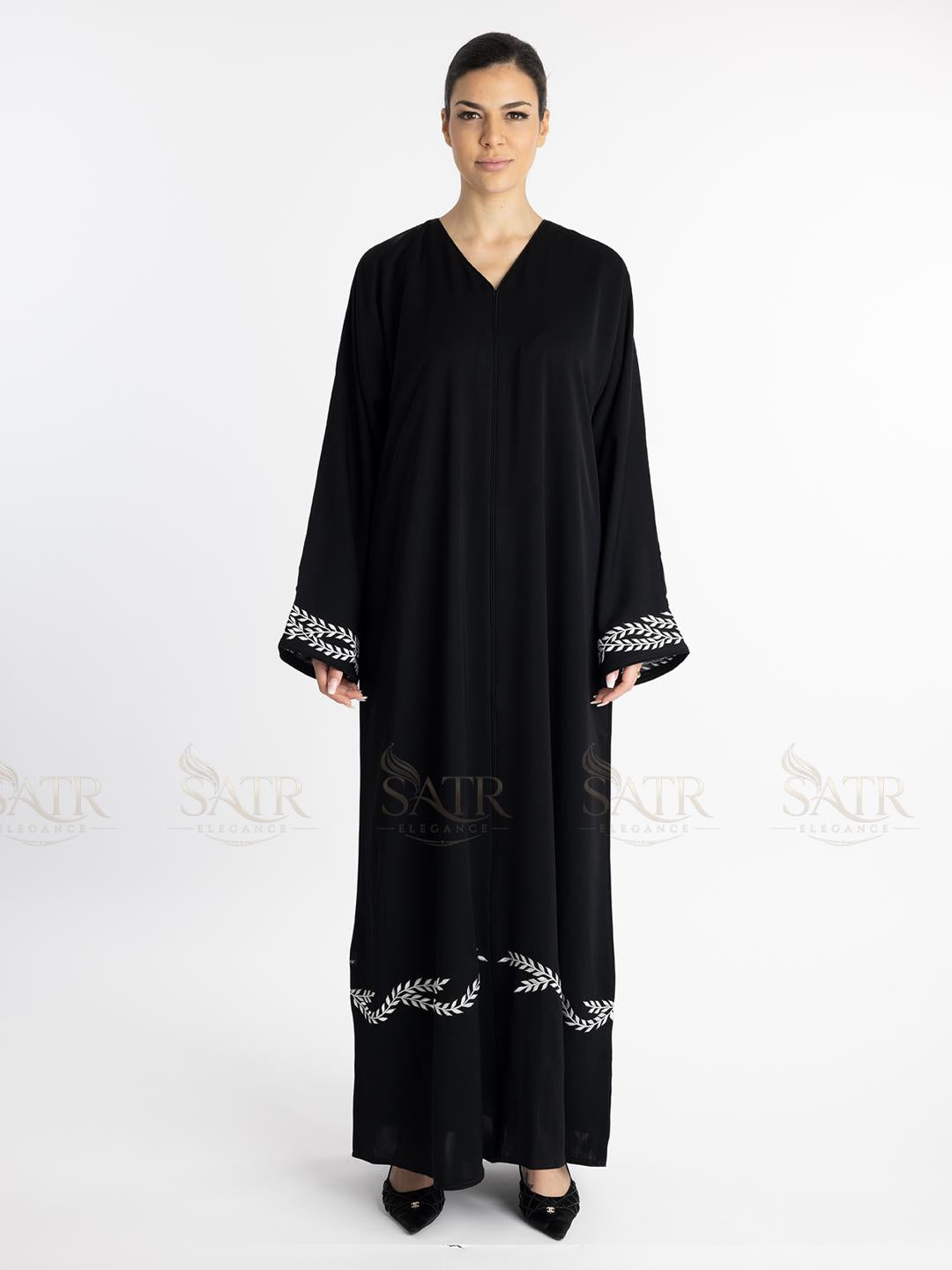 Woman wearing a premium black abaya with white embroidery on a white background