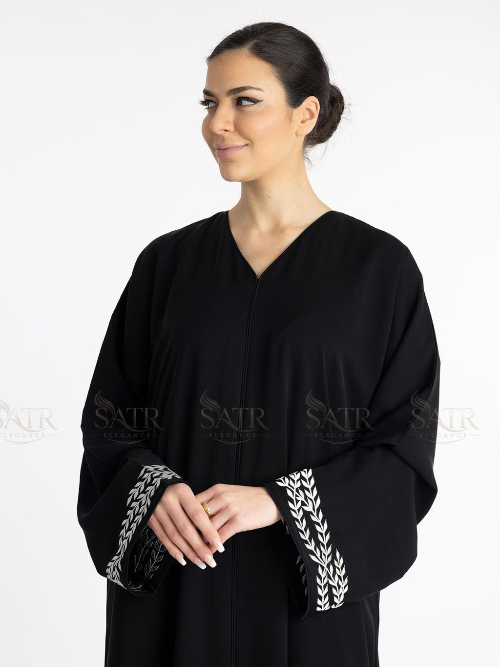 Woman wearing a premium black abaya with white embroidery on a white background