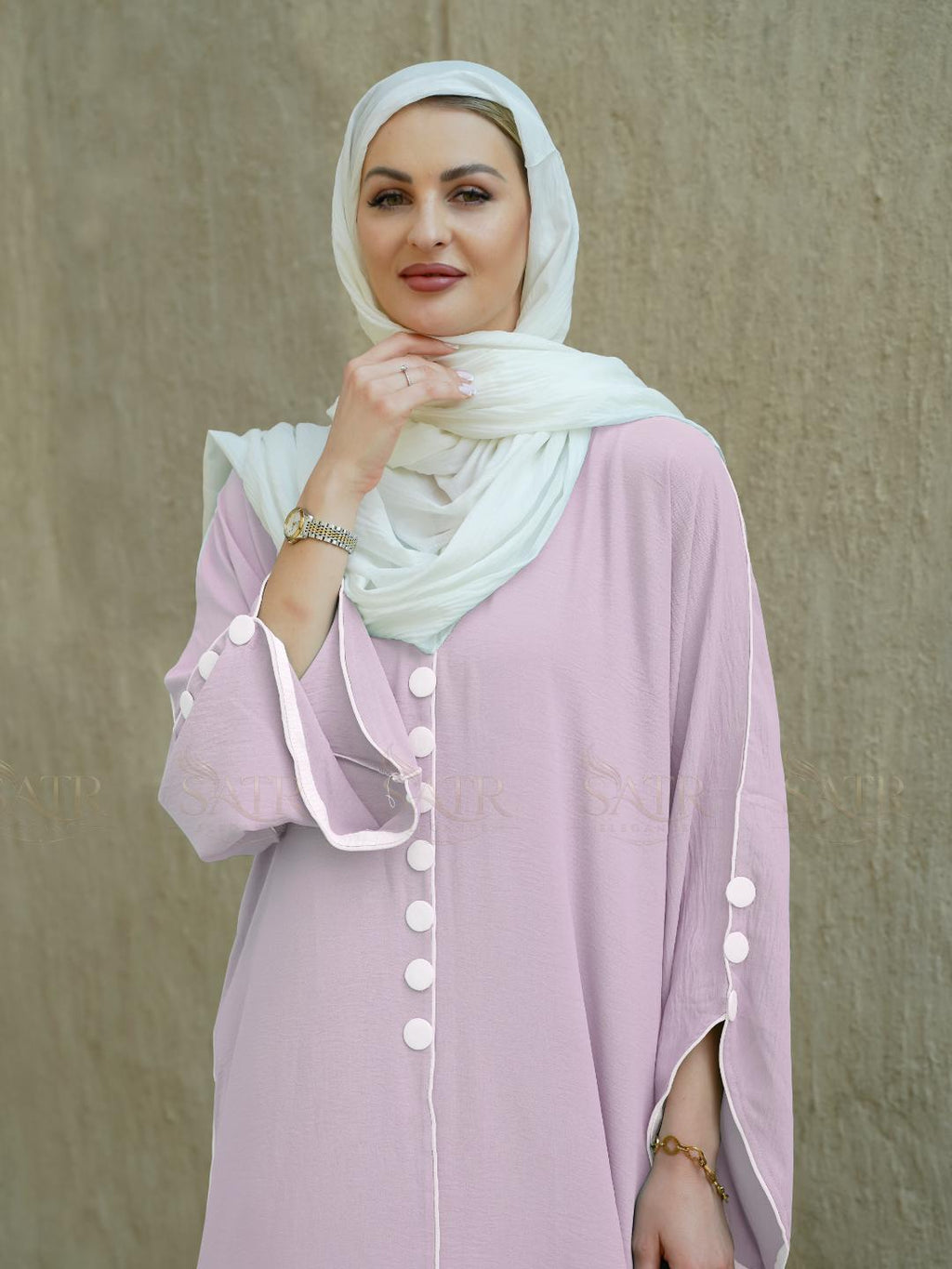Woman wearing a light pink outfit with a white hijab against a beige background