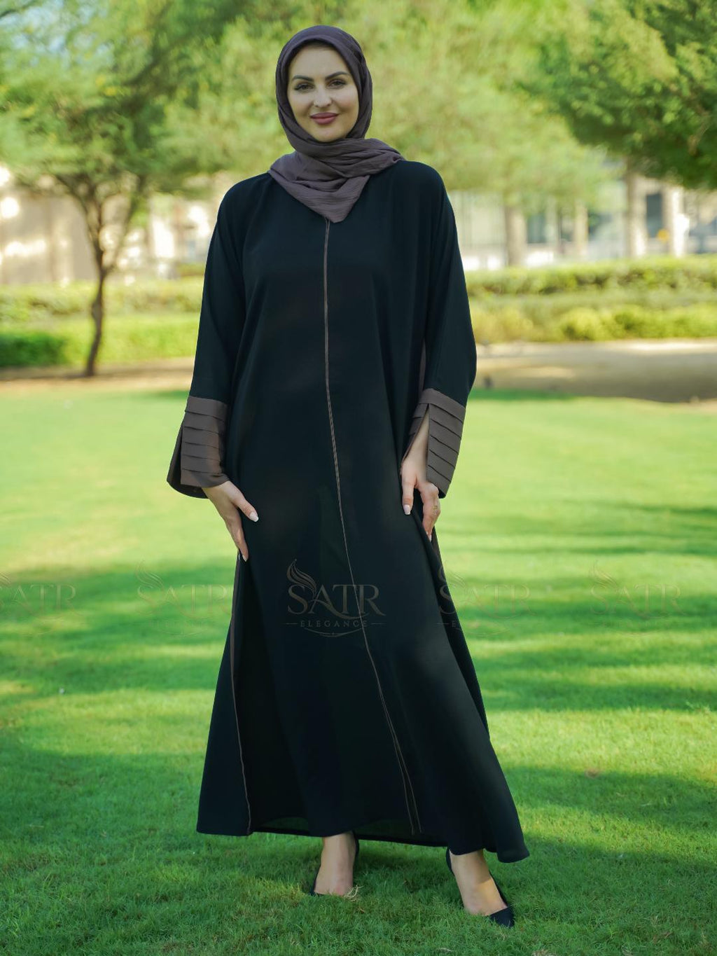 Woman wearing a black abaya with brown accents in a park setting