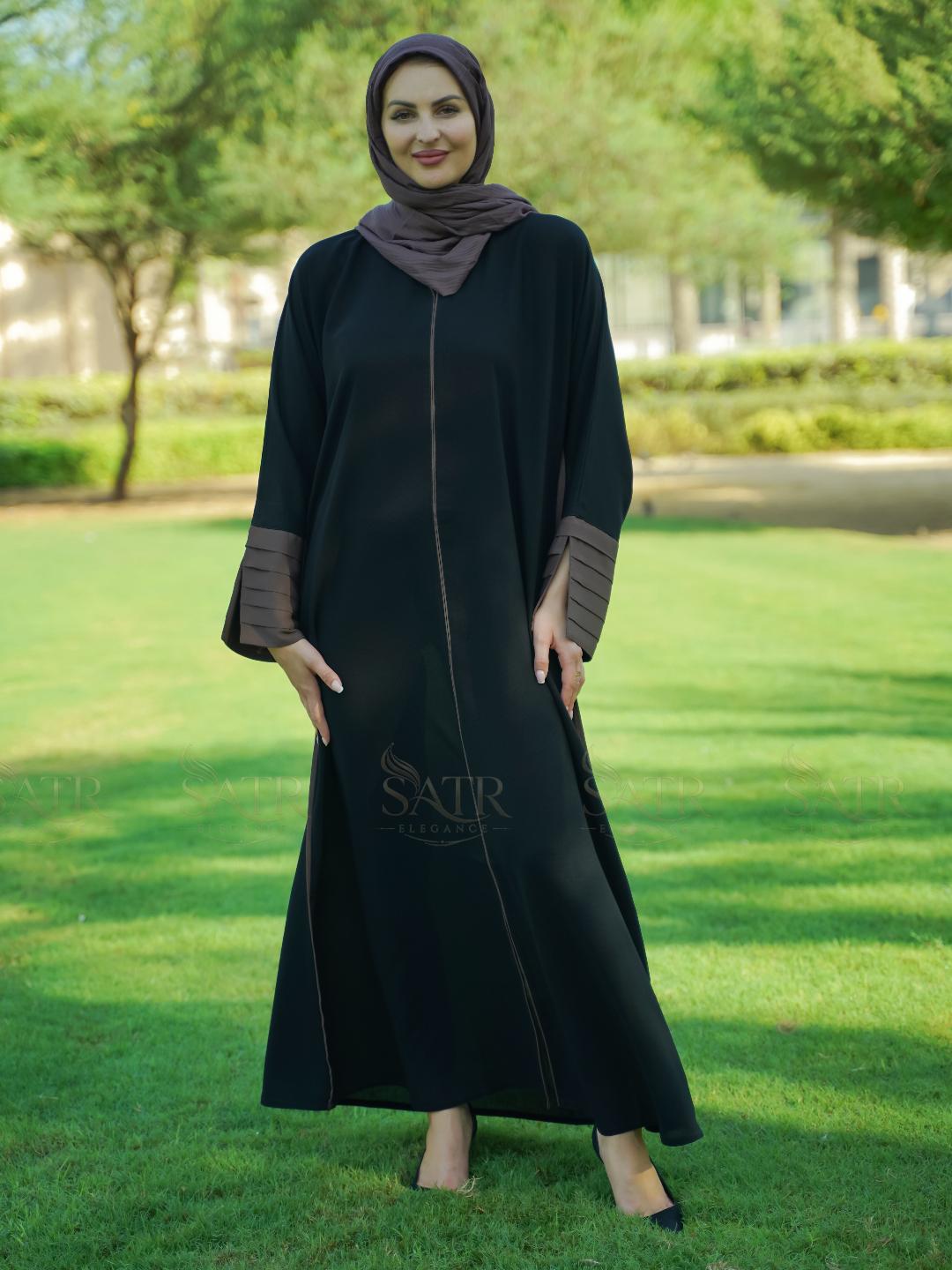Woman wearing a black abaya with brown accents in a park setting