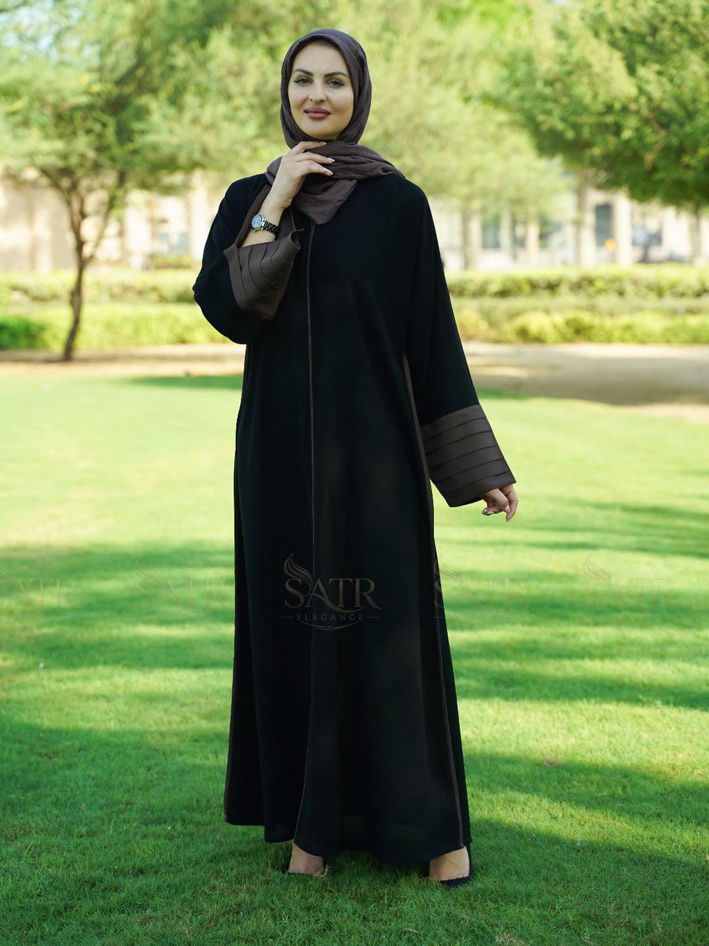 Woman wearing a black abaya with brown trim in a park setting