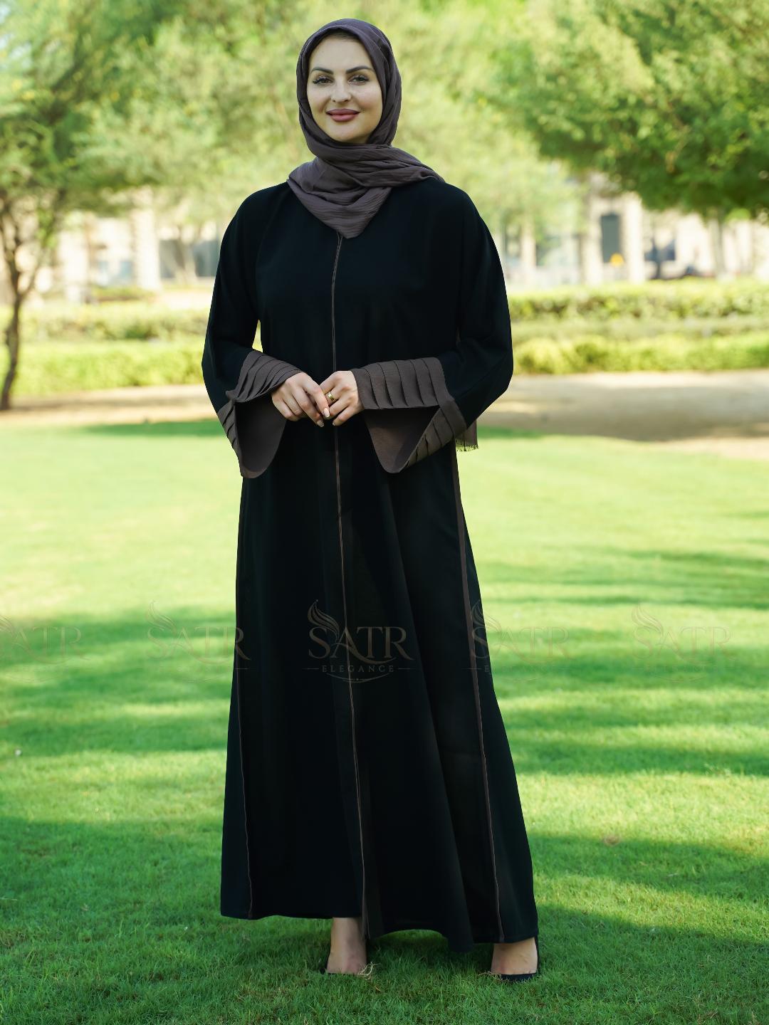 Woman in a black abaya with a brown hijab standing on grass with trees in the background